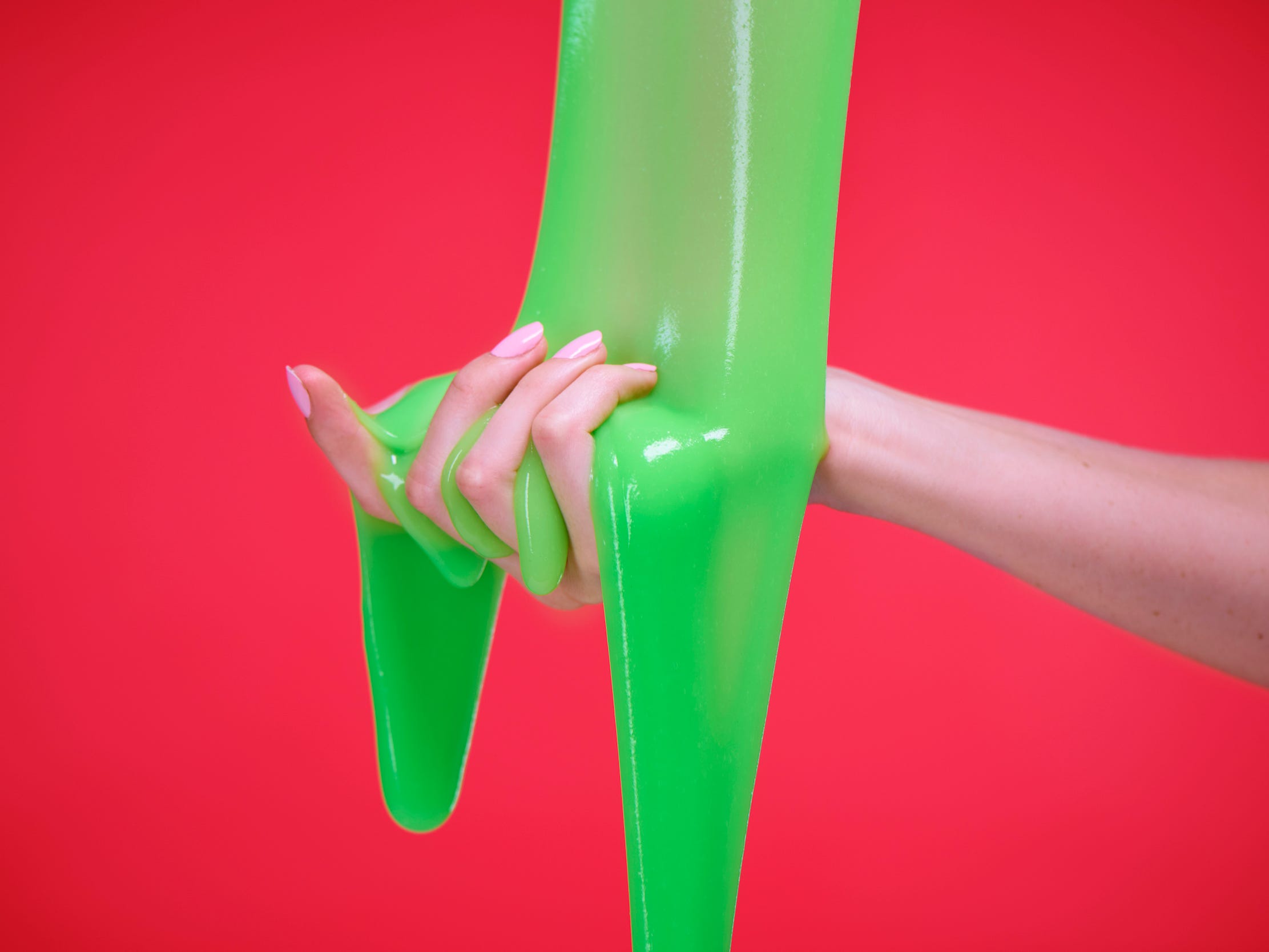 Hand playing with green slime on a red background.