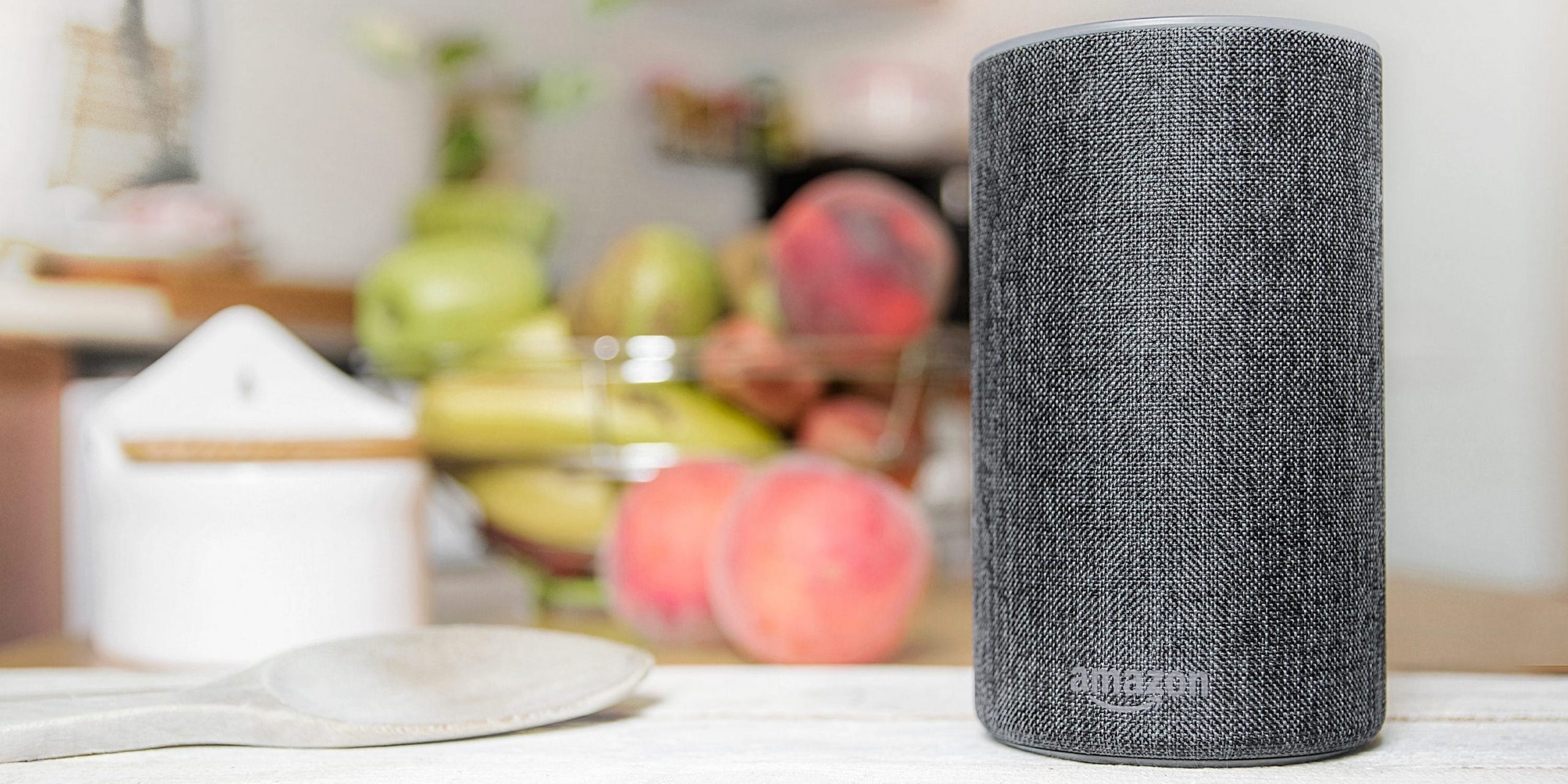 An Amazon Echo in a kitchen, sitting next to fruit and spoons.