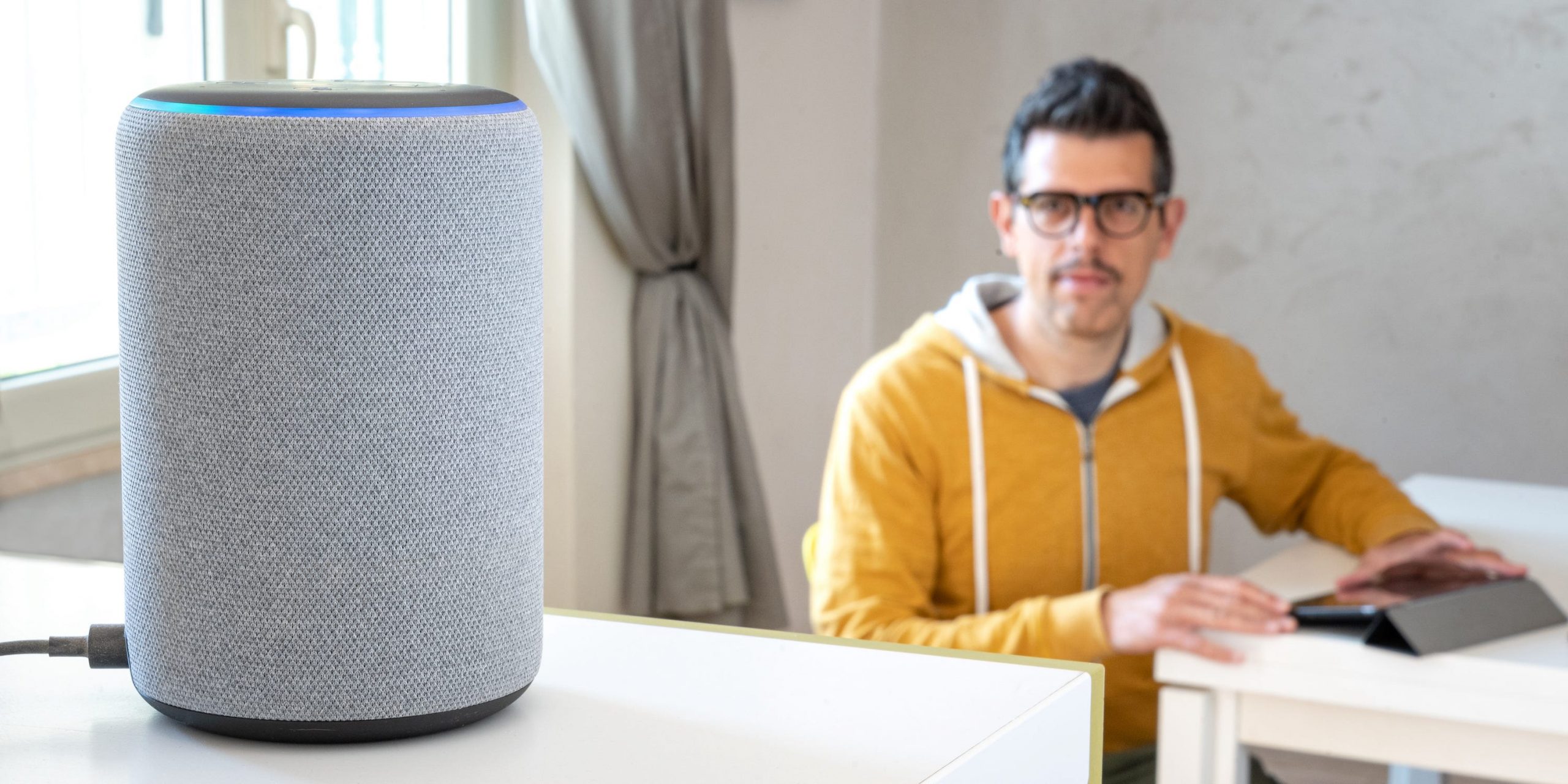 An Amazon Echo sitting on a table, with a man looking at it