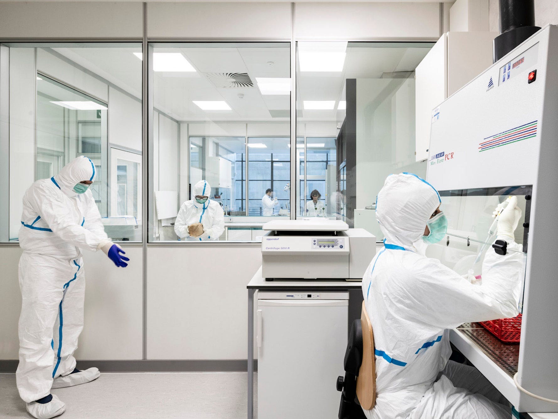 Scientists wearing hite protective jumpsuits masks are in a laboratory.