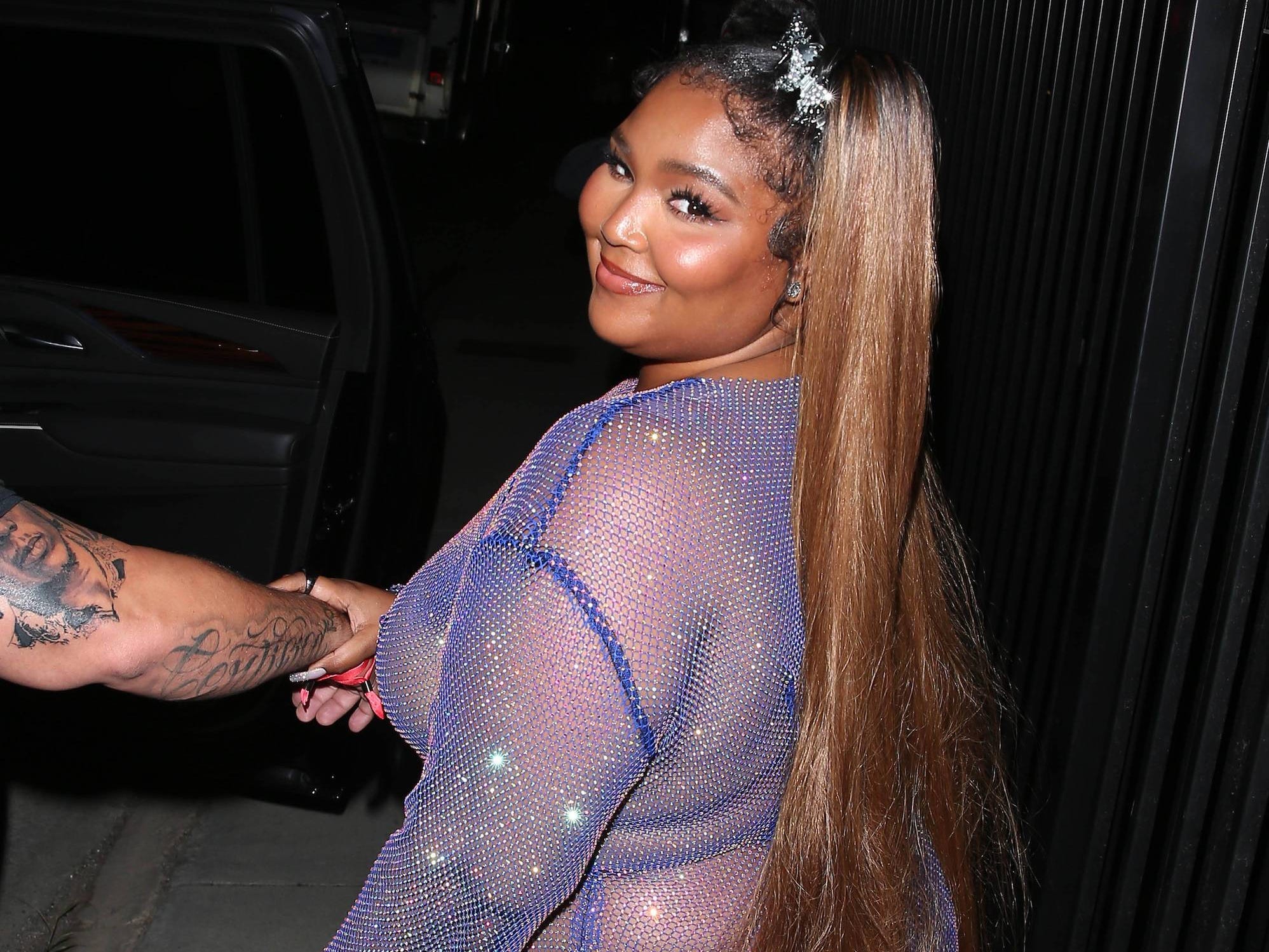 Lizzo smiles for a photo wearing a see-through dress.