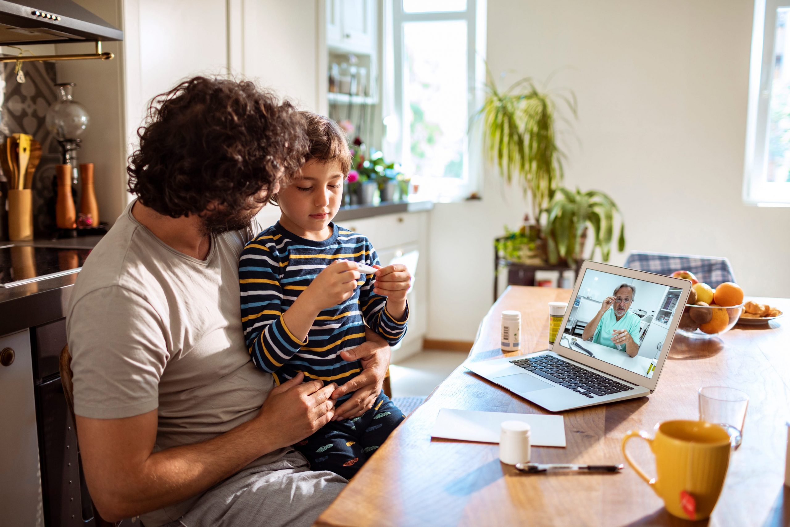 Close up of a father with his son in the lap consulting with the doctor over a laptop