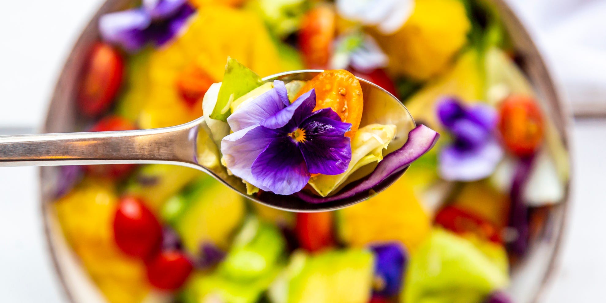 A spoon and bowl of salad with an edible flower.