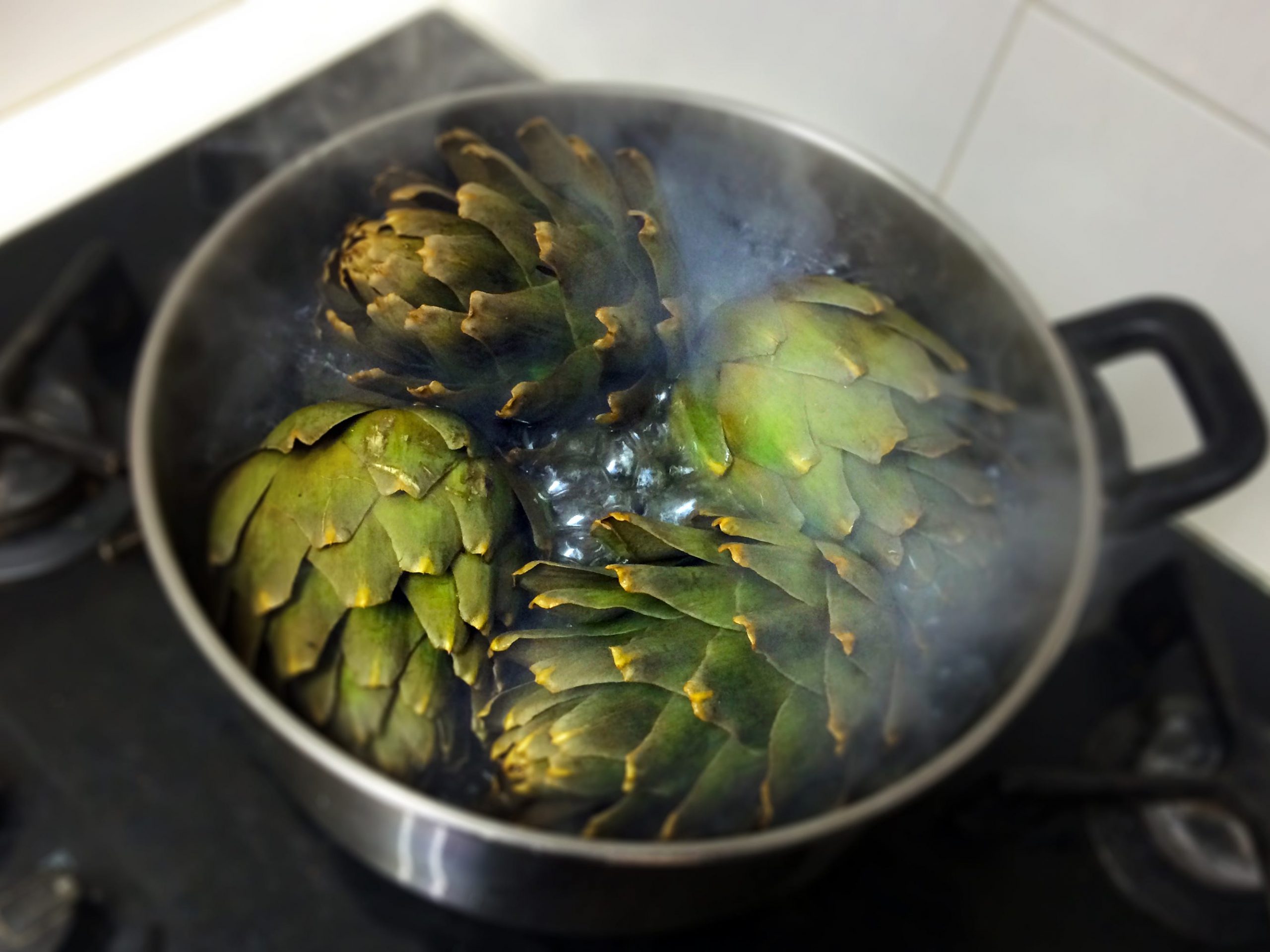 Four artichokes boiling in a pot of water