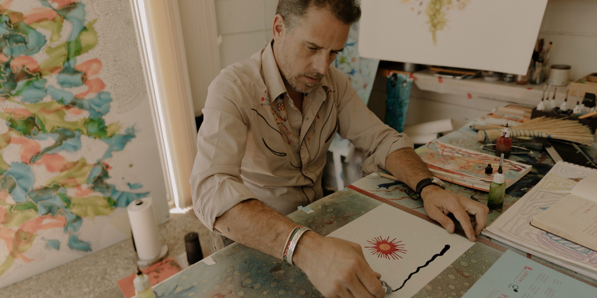 Hunter Biden paints in a studio, surrounded by works of art.