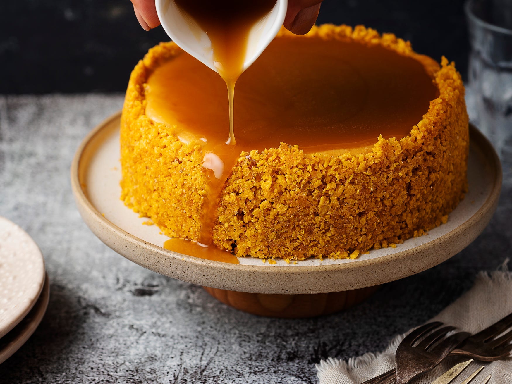 Caramel sauce being poured overtop a cheesecake with a graham cracker crust