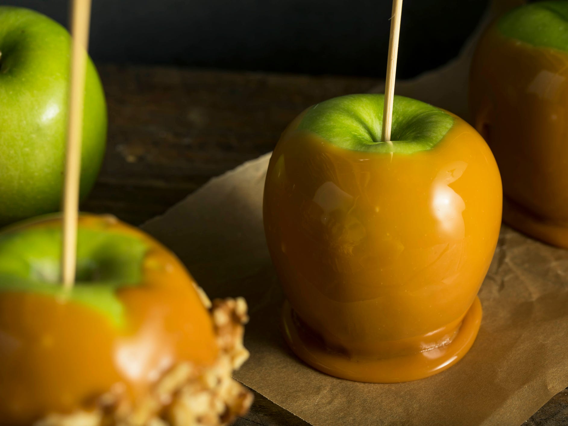 Three bright green apples dipped in caramel coating drying on parchment paper