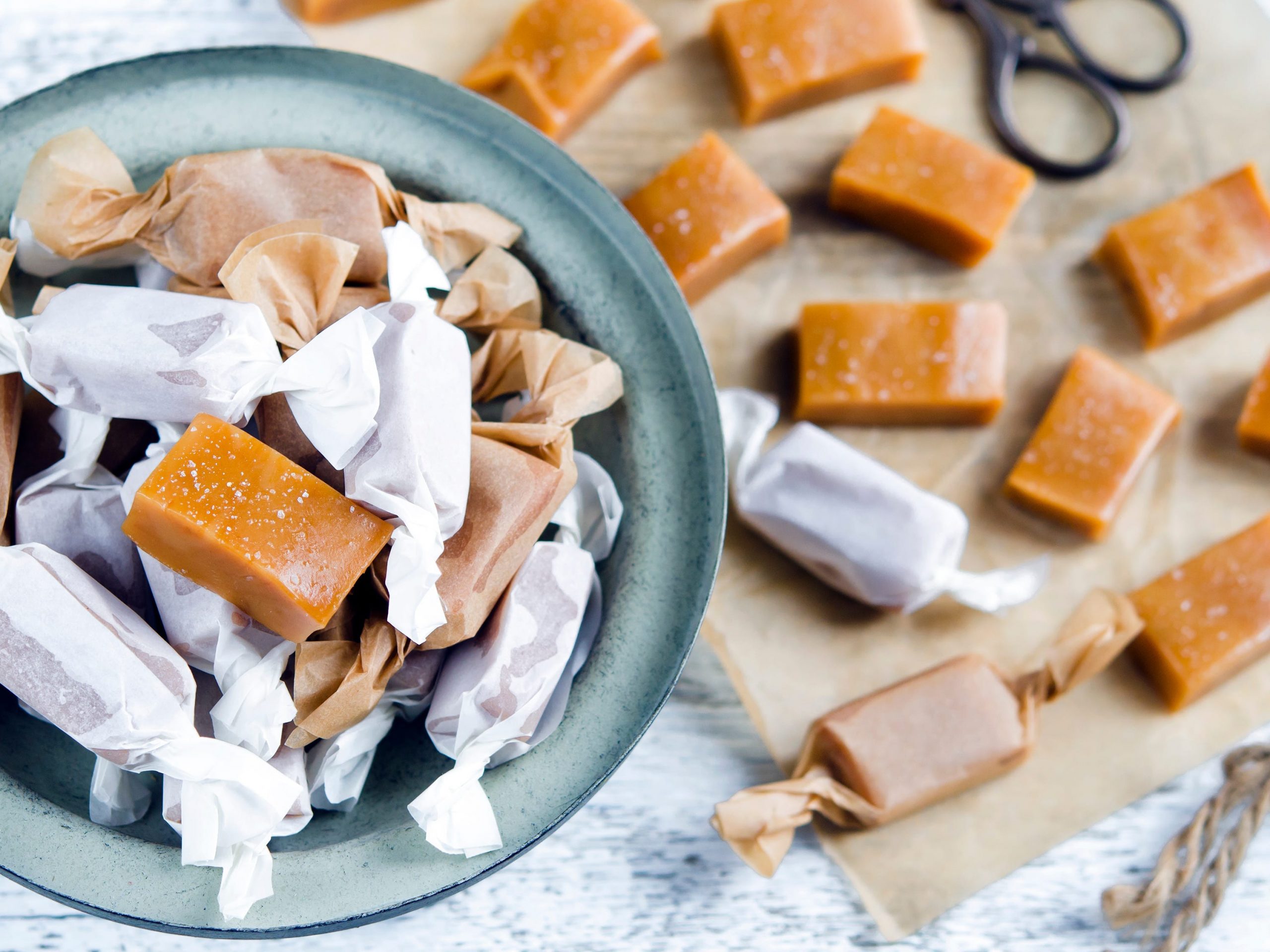 A bowl of homemade chewy caramel candies with several more unwrapped in the background