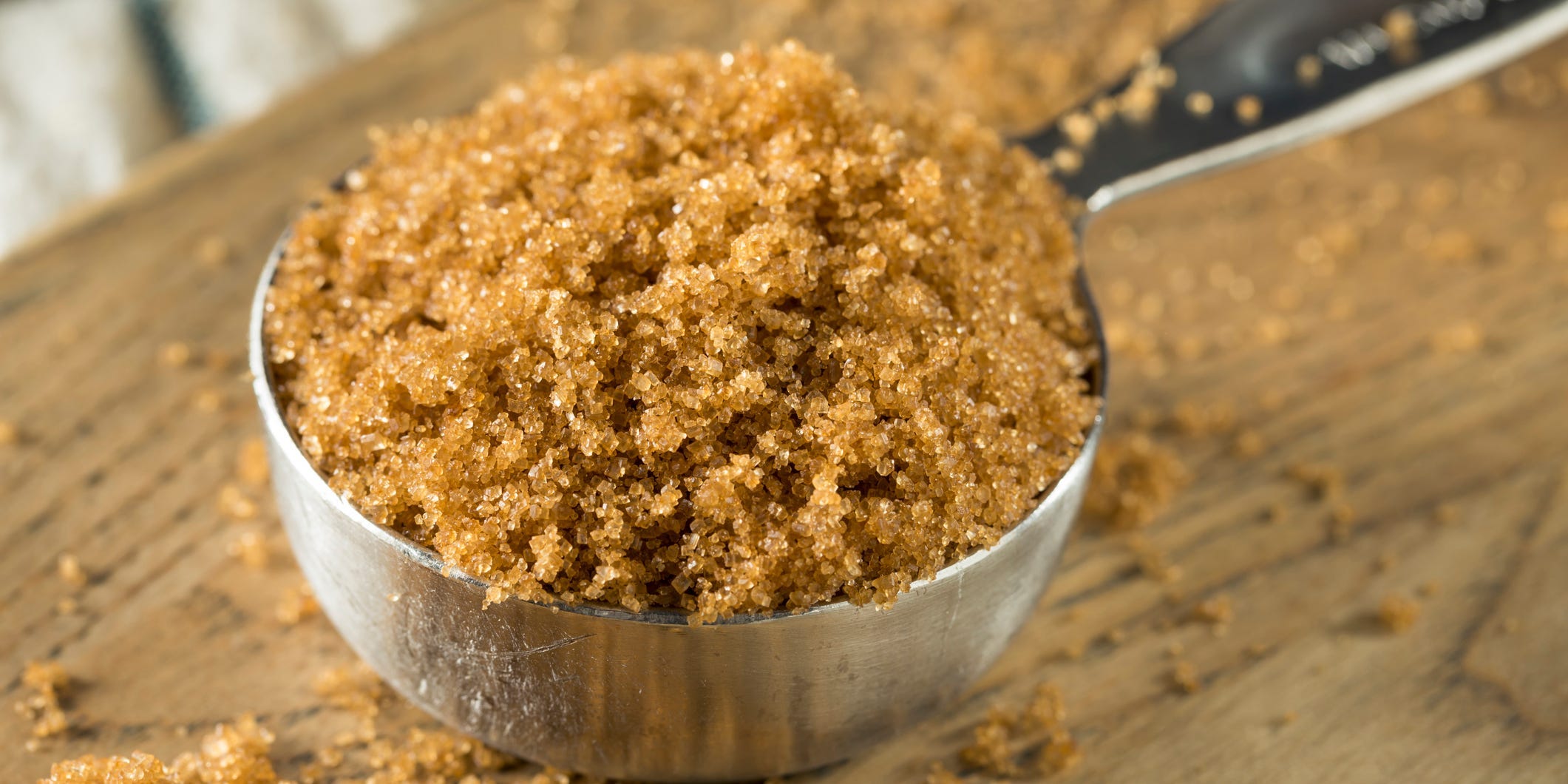 A measuring cup of brown sugar on a wooden cutting board