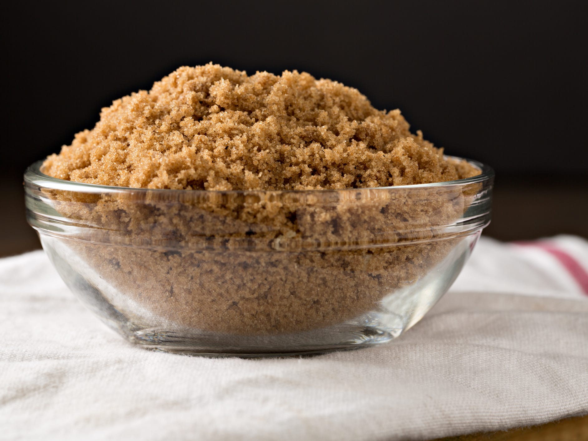 A clear glass bowl of brown sugar sitting on a white tea towel