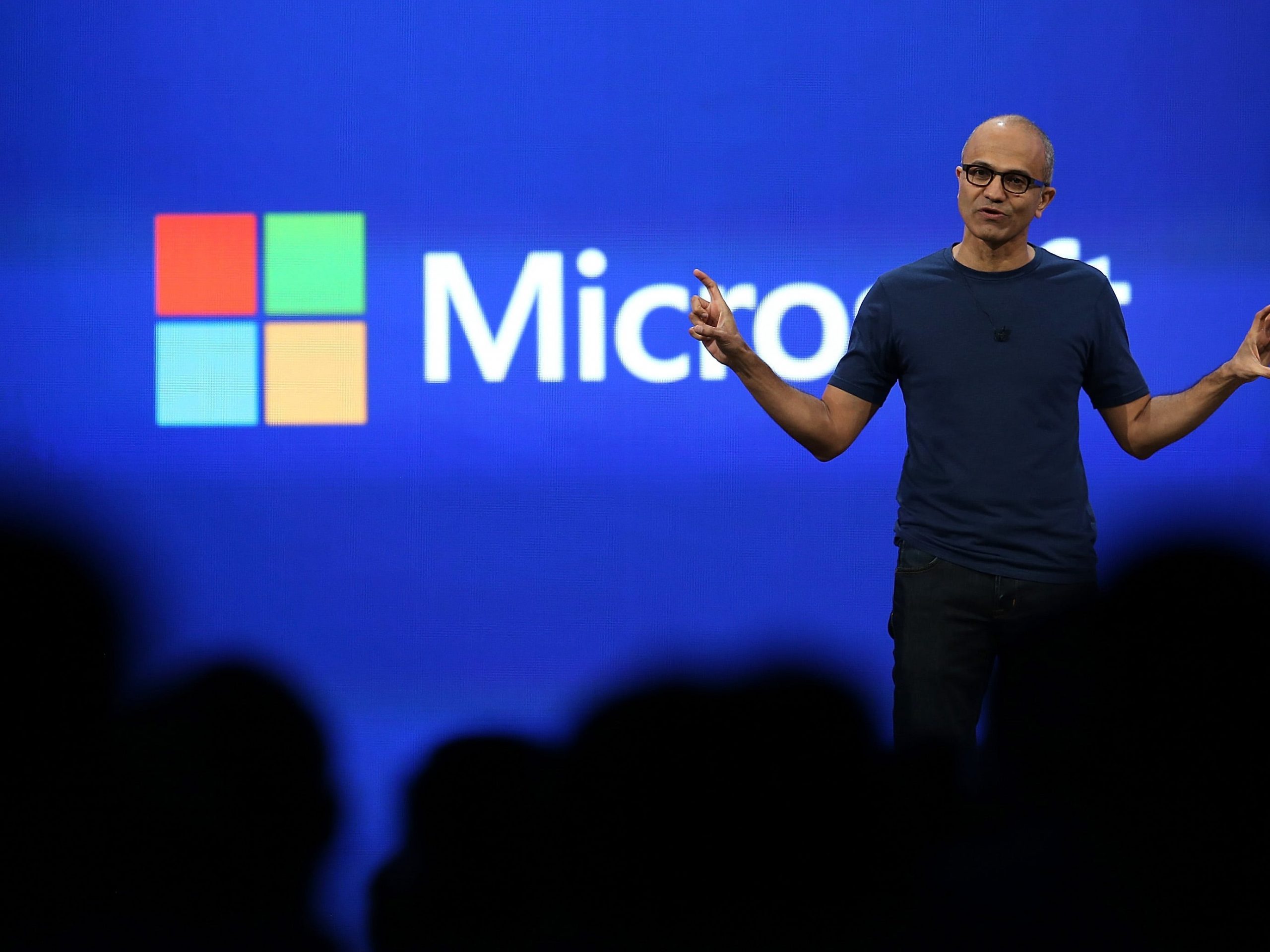 Microsoft CEO Satya Nadella stands on stage and gestures widely with both hands