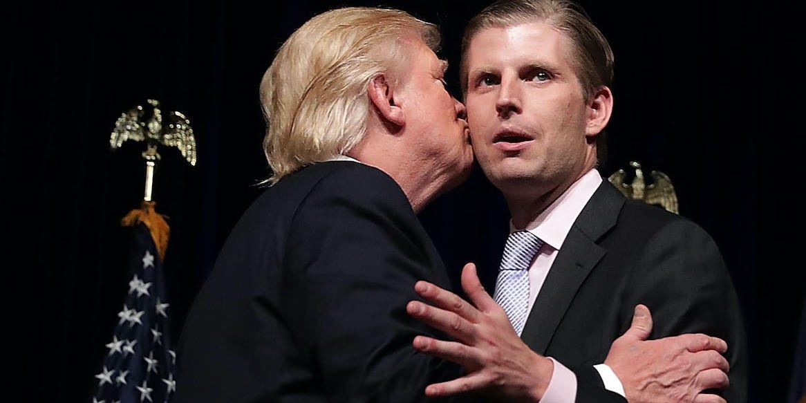 Donald Trump kisses his son, Eric, on the cheek on-stage at a campaign rally while Eric looks away into the distance.