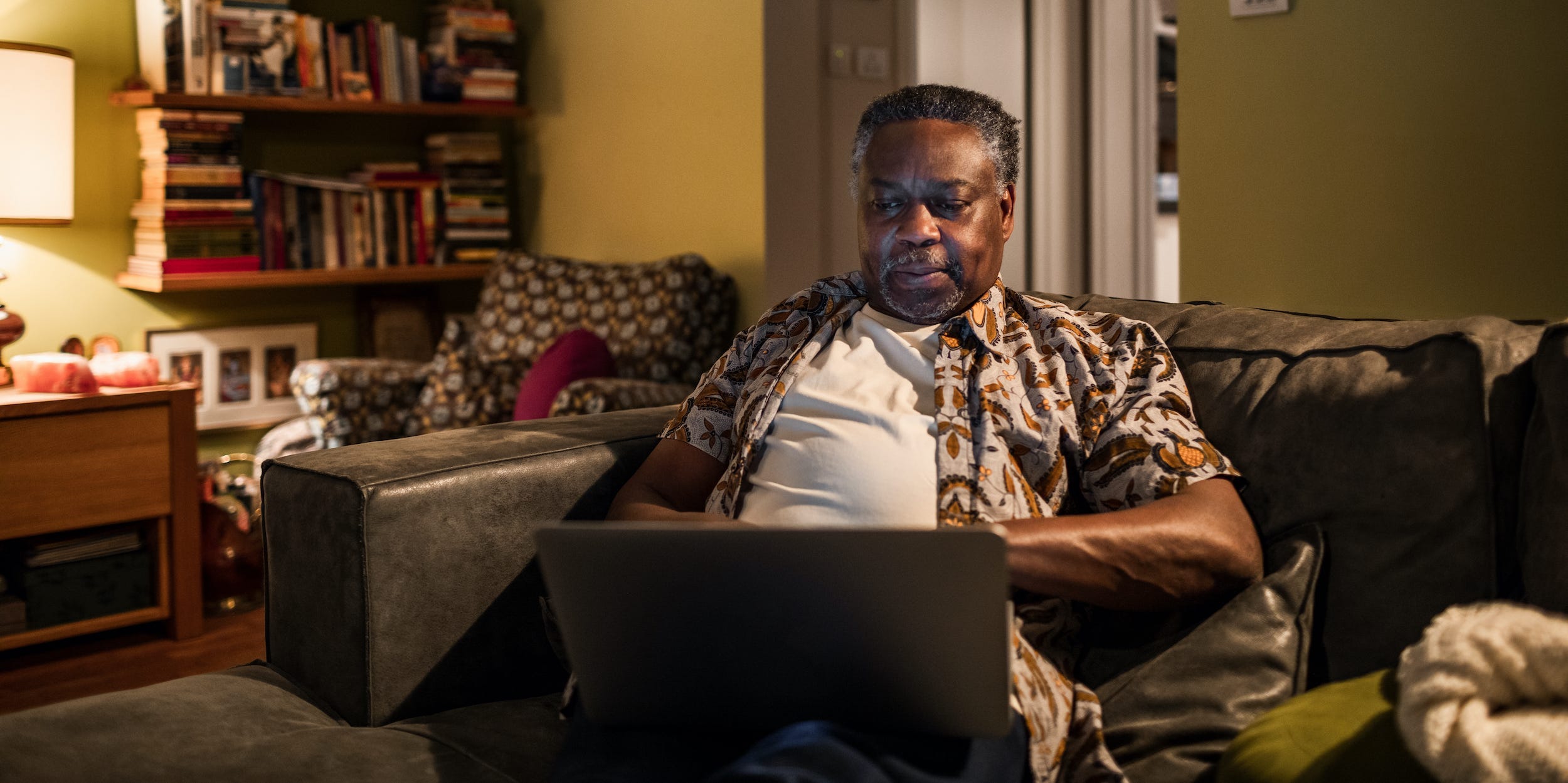 senior man looking at laptop on couch at home