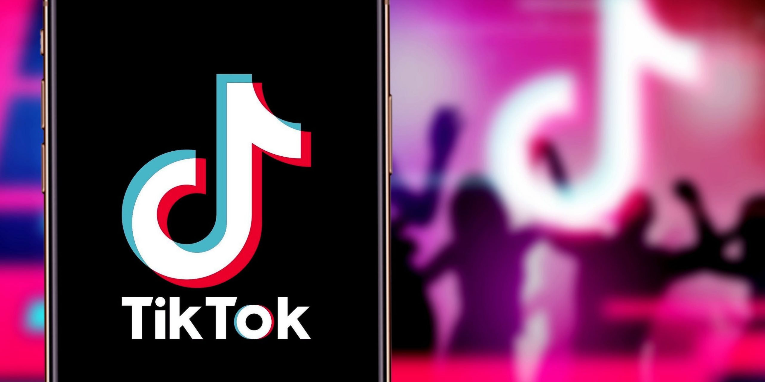 An iPhone displaying the TikTok logo. In the background, silhouettes dance around a TikTok logo.