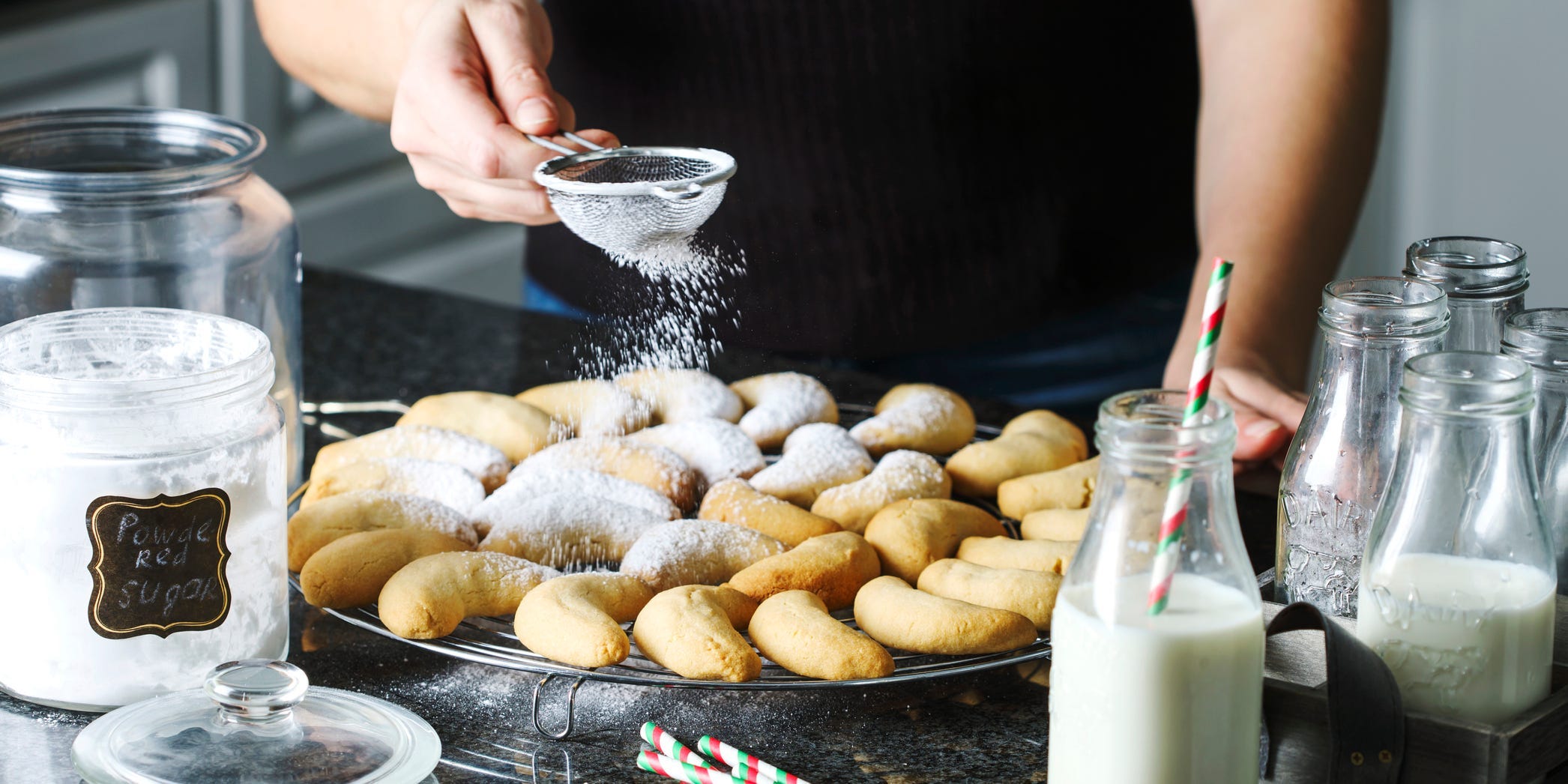 Someone sprinkling powdered sugar over some cookies.