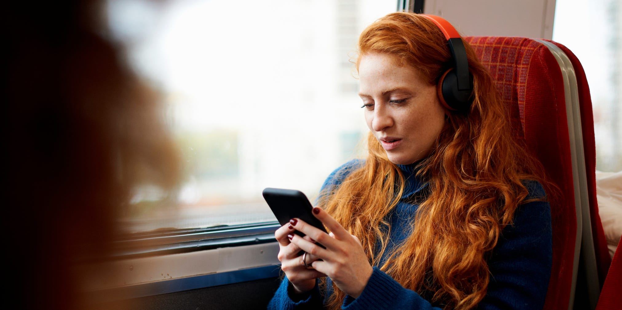 woman on train looking at phone headphones