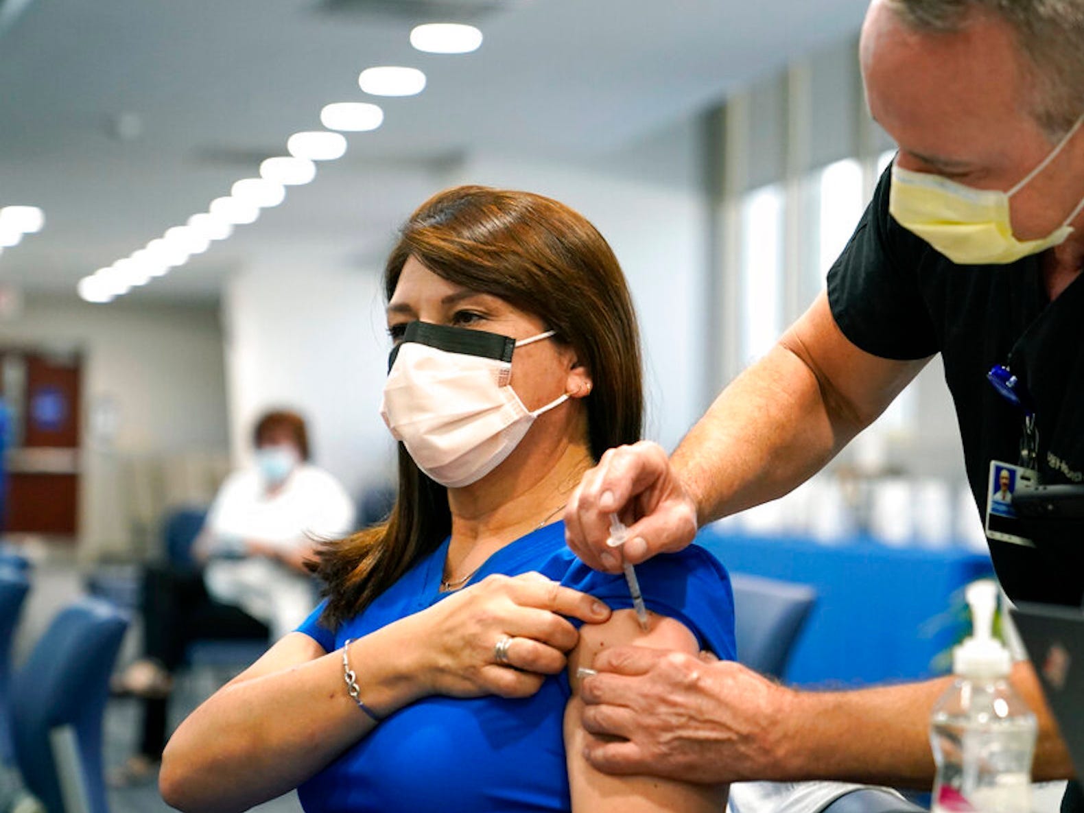 A woman wearing a mask and blue scrubs gets a shot in a clinic.