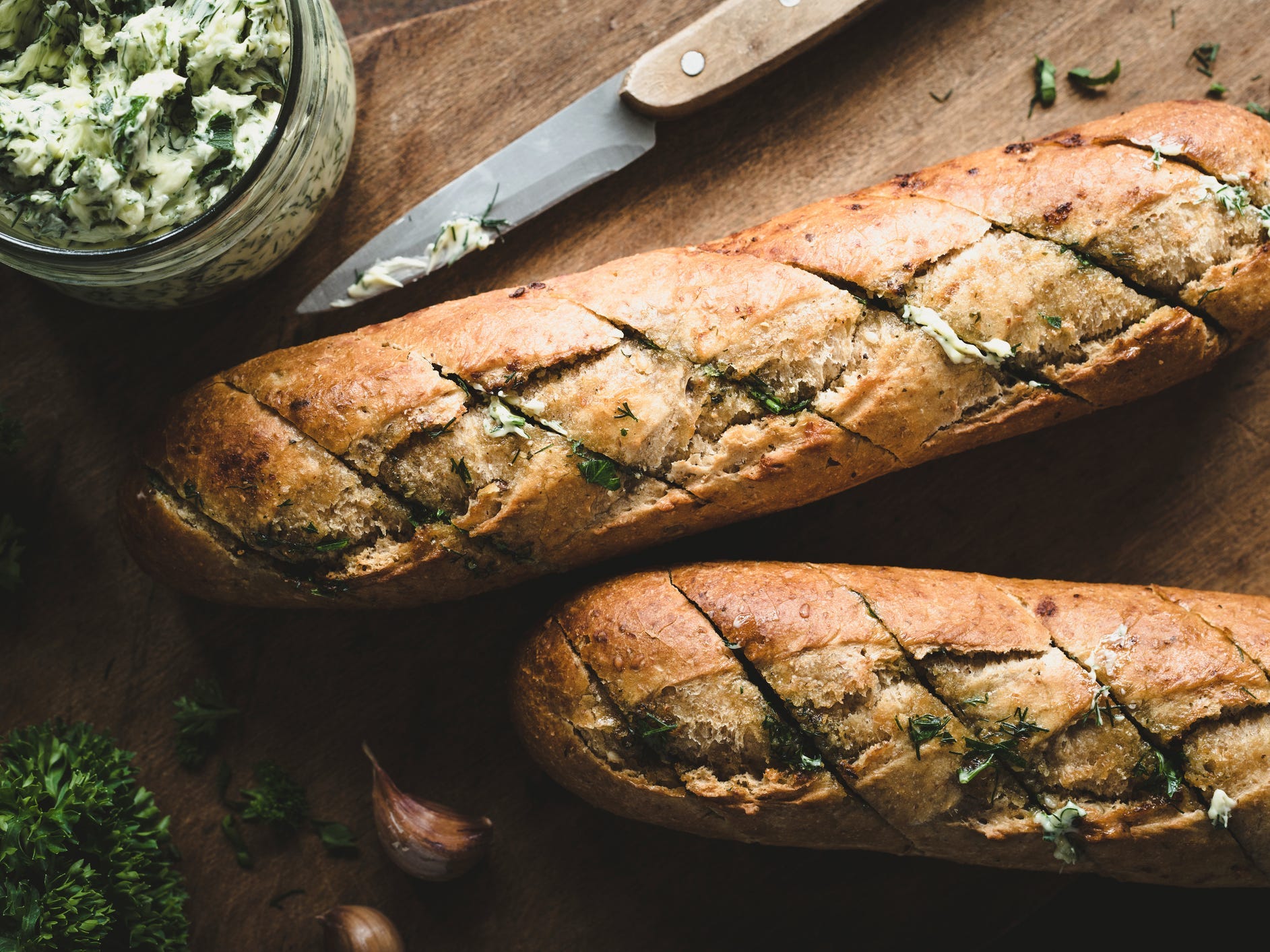 Two loaves of bread with slits sliced into them that are stuffed with garlic butter