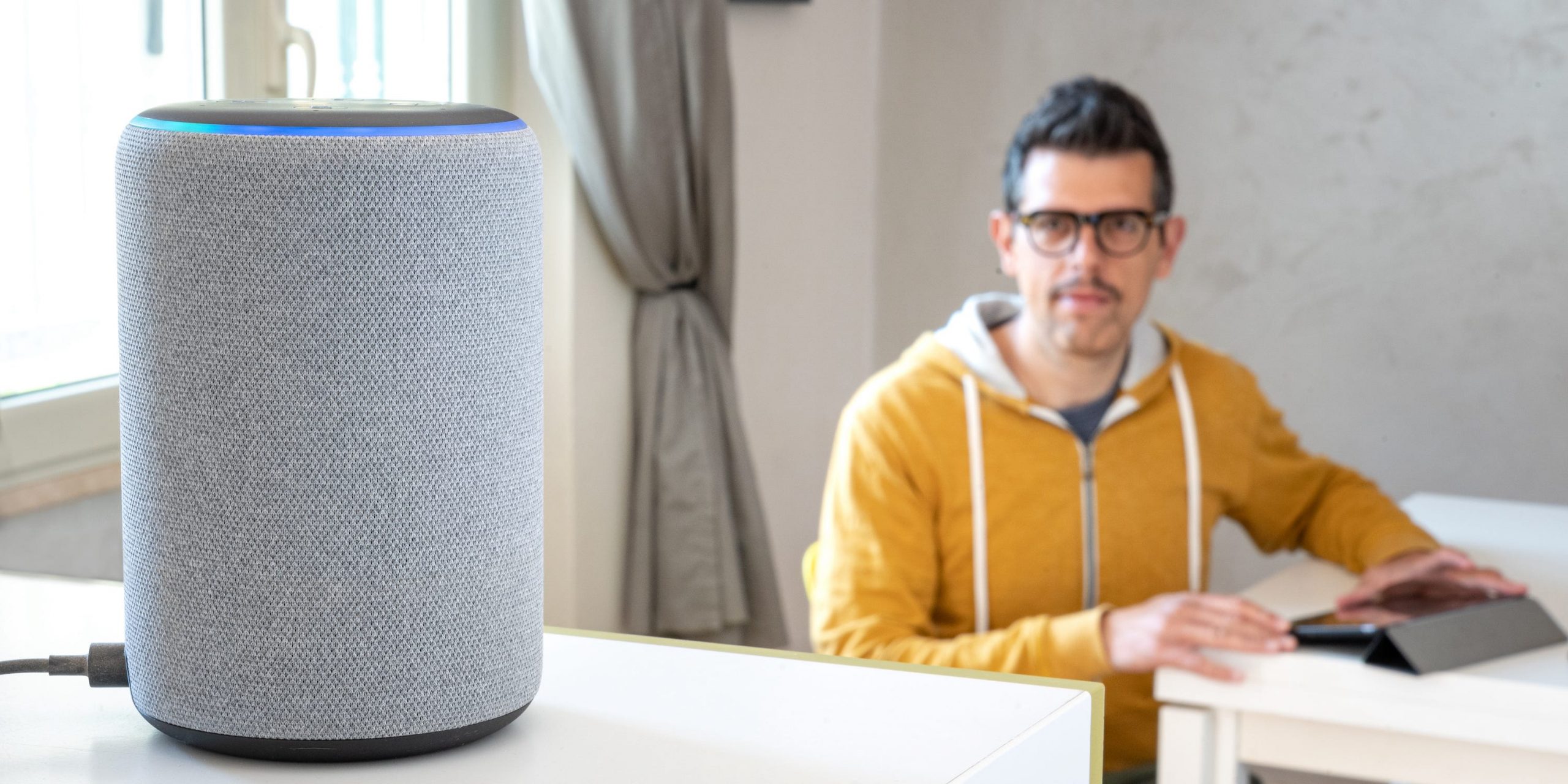 An Amazon Echo sitting on a table, with a man looking at it