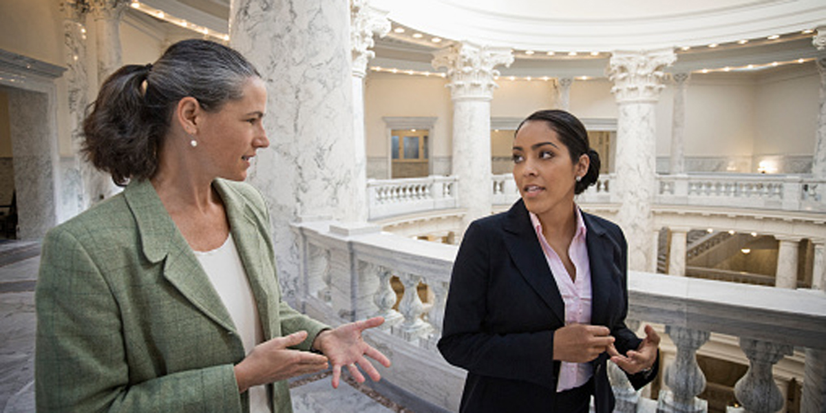 Two women in suits talking and walking through the US capitol building.