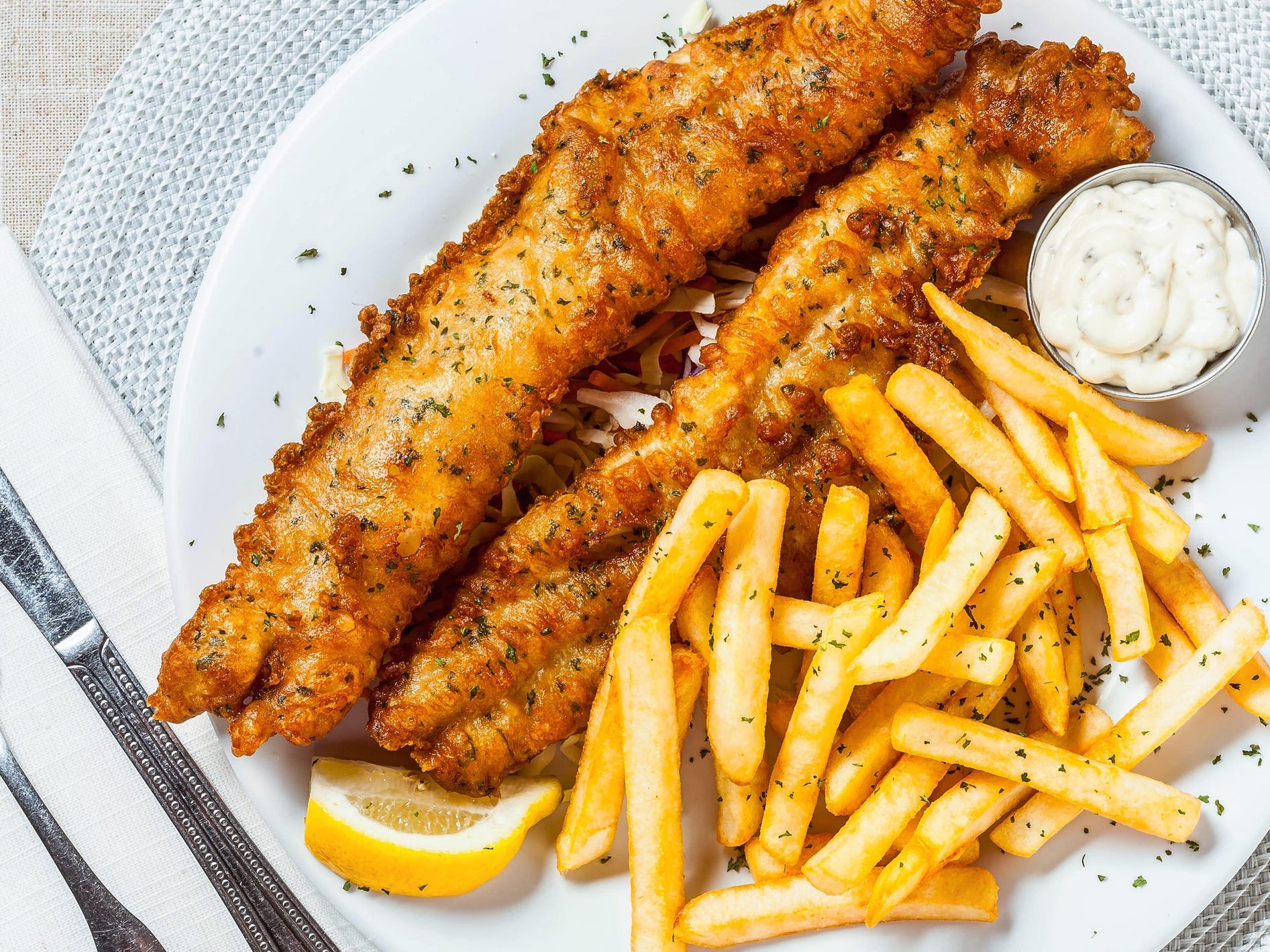 A top-down view of a plate of fish and chips with a side of tartar sauce