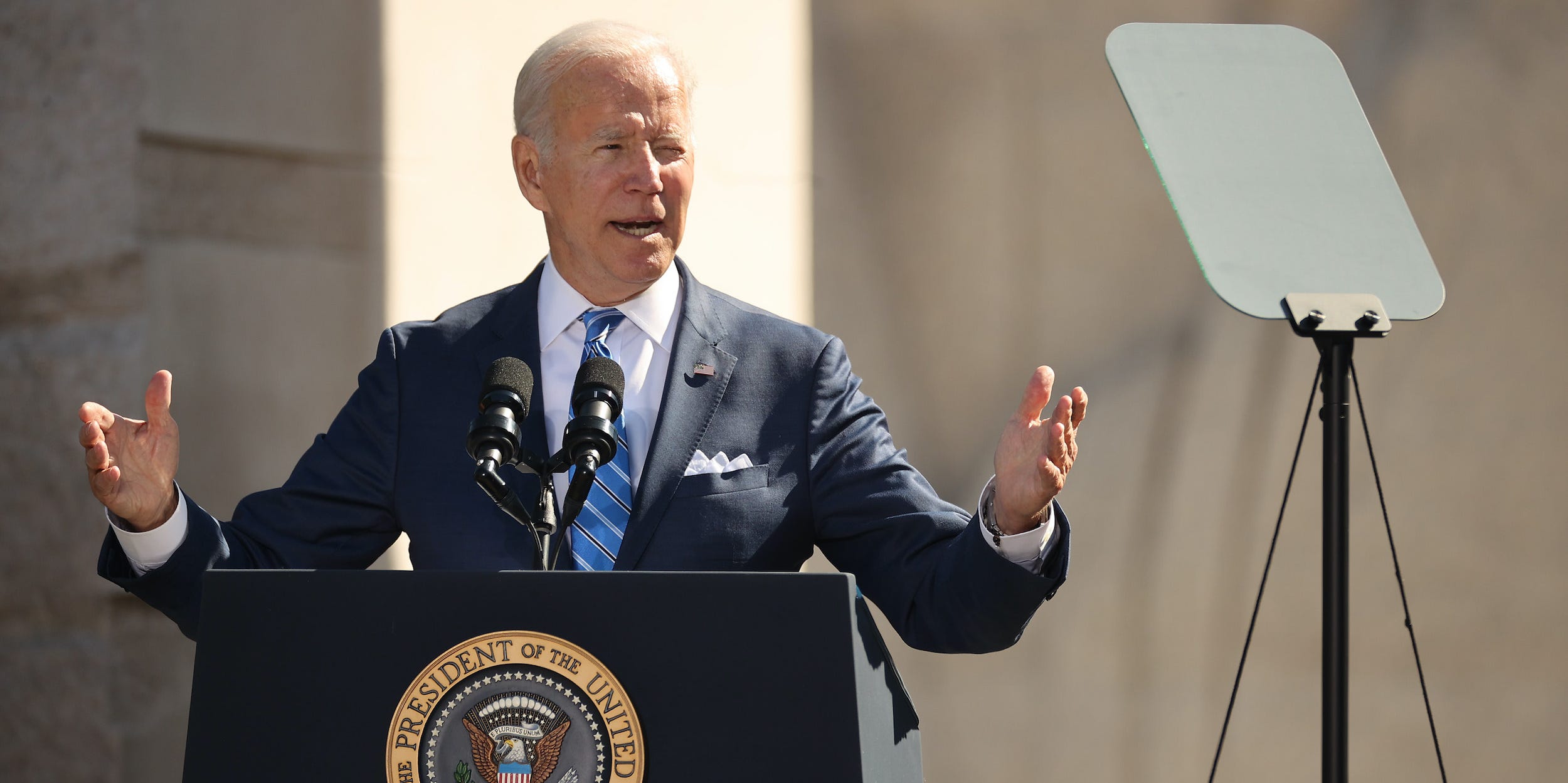 President Joe Biden speaks in front of the Martin Luther King Jr. memorial, gesturing with open palms to his sides while looking toward a teleprompter.