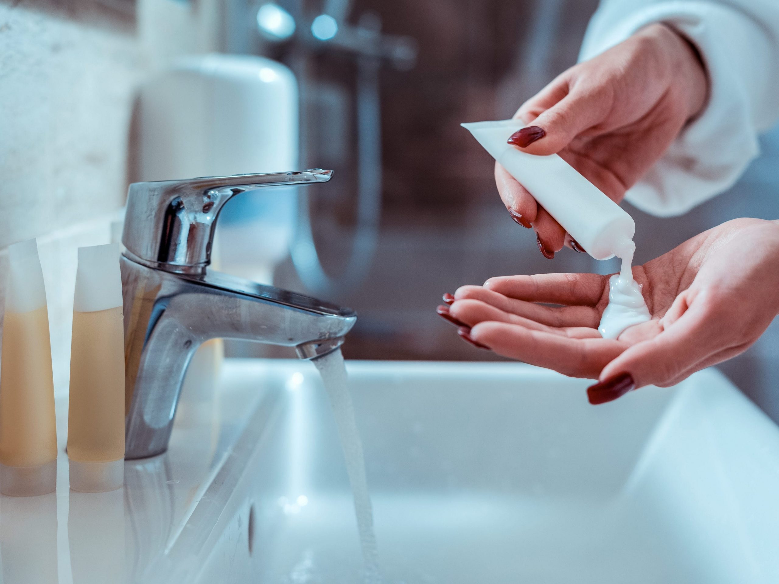 person squeezing skincare product in hands over sink to wash face