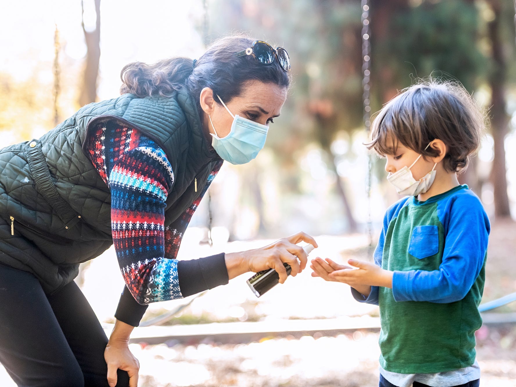 a woman wearing a mask puts hand sanitizer on a child's hands