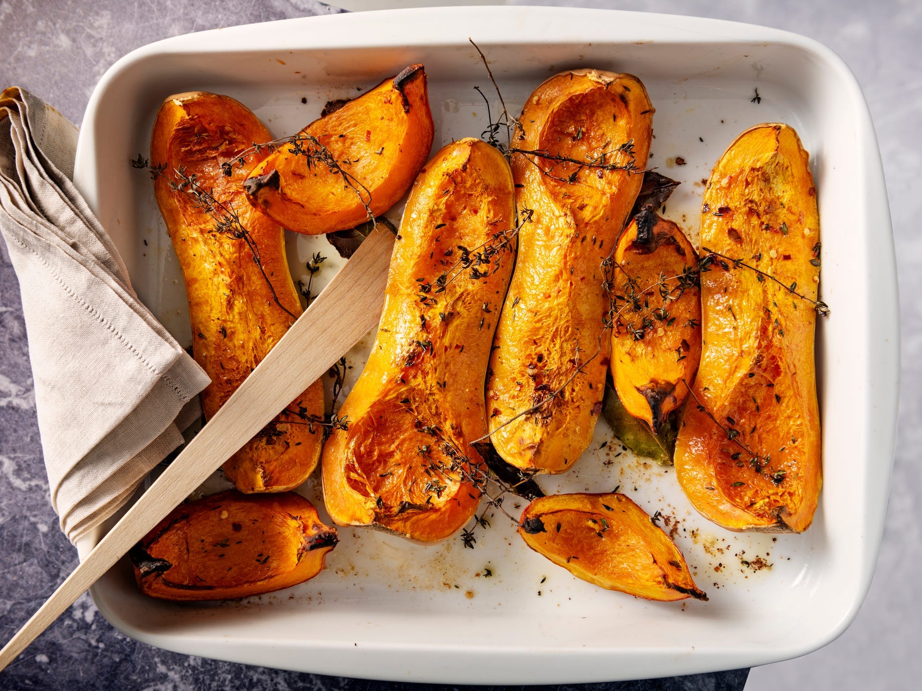 A roasting dish full of quartered and roasted butternut squash topped with herbs