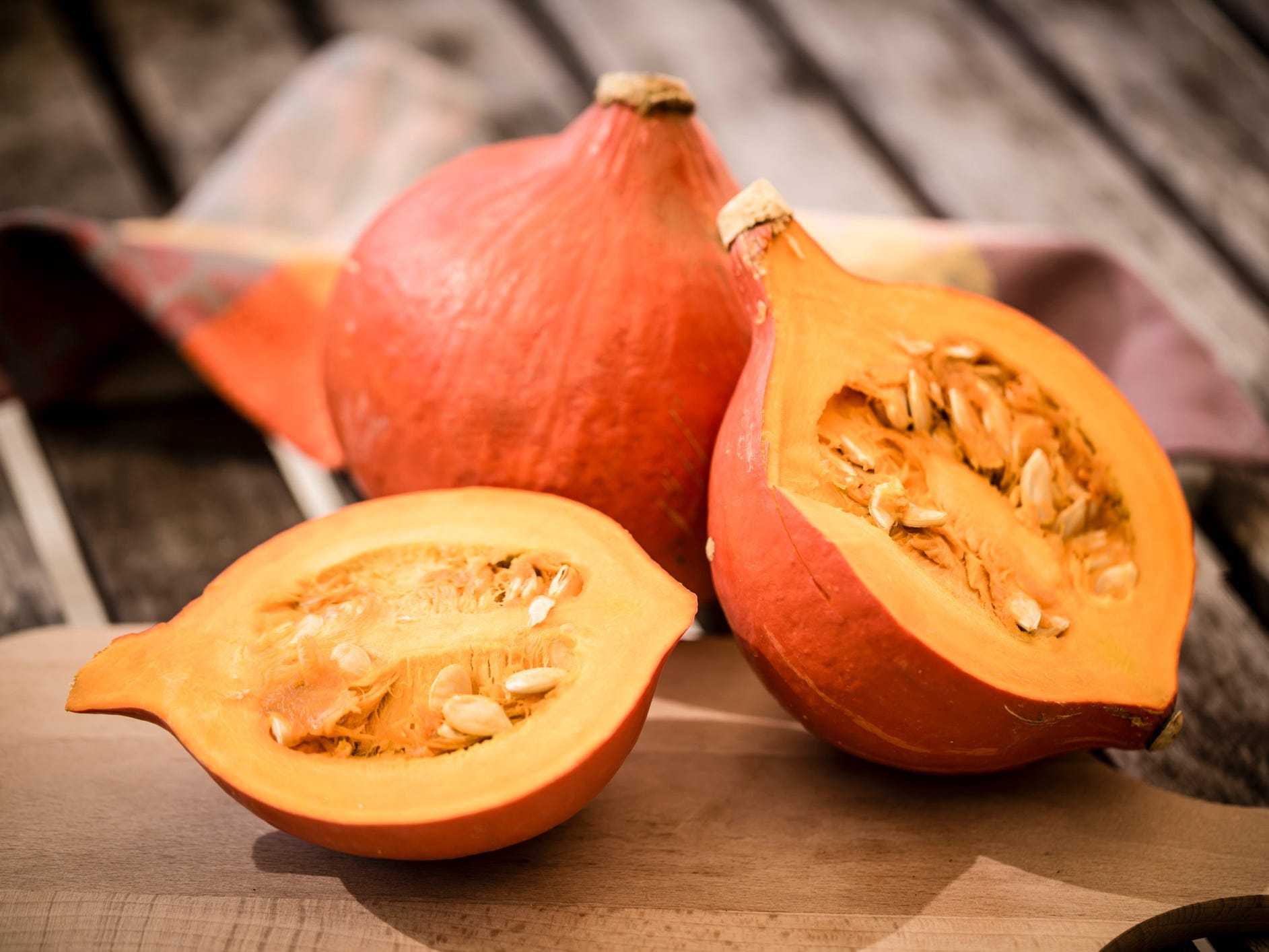 A raw red kuri squash cut in half sitting in front of a whole one