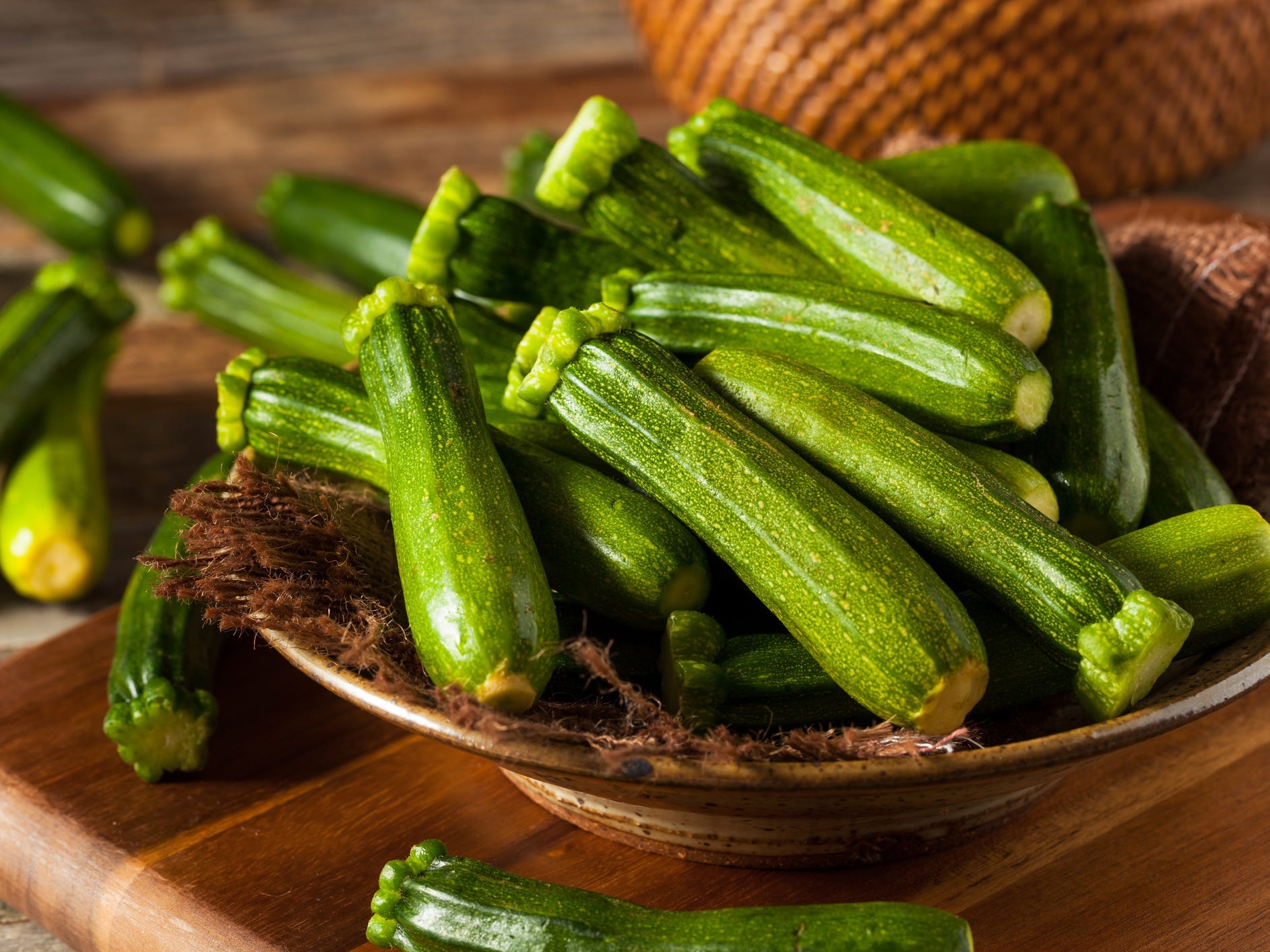 A wooden bowl full of whole, raw zucchini