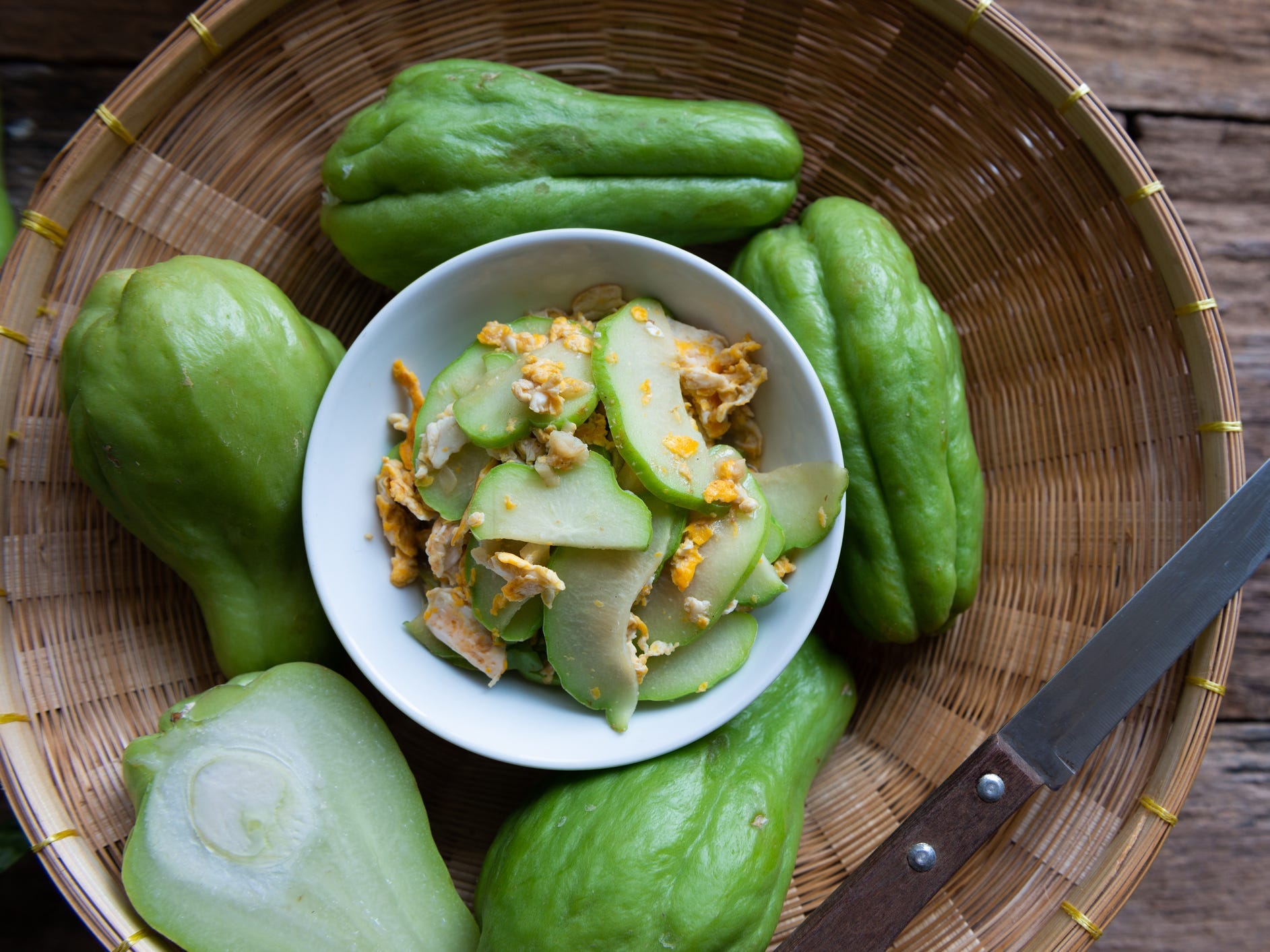 Whole and halved chayote squash surrounding a bowl of cut up and sauteed chayote