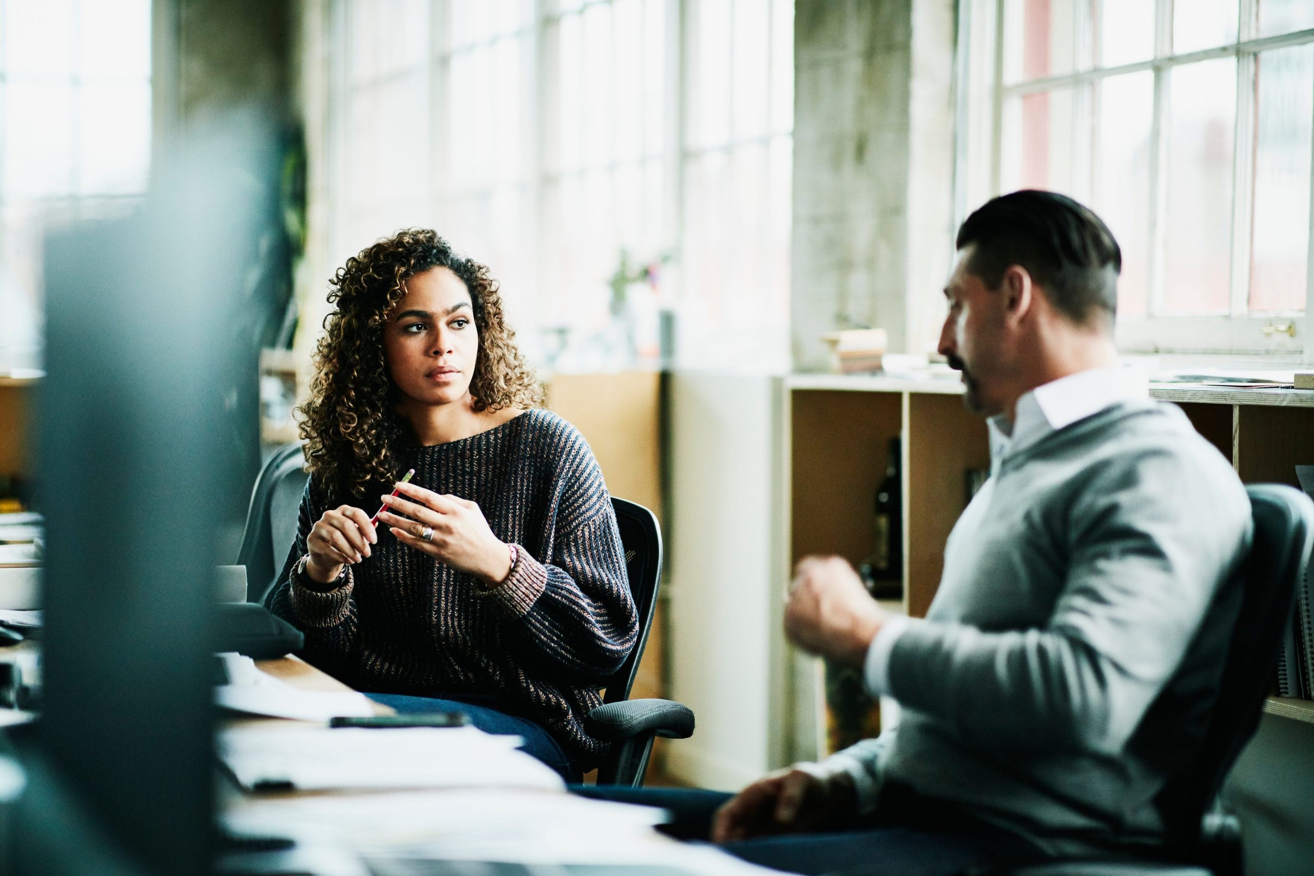 Coworkers, a Latina female and white male, in discussion while in a meeting.