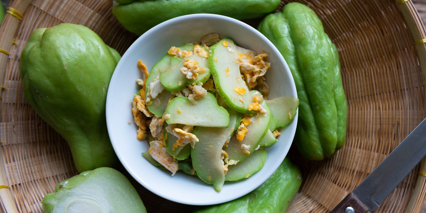 Whole and halved chayote squash surrounding a bowl of cut up and sauteed chayote