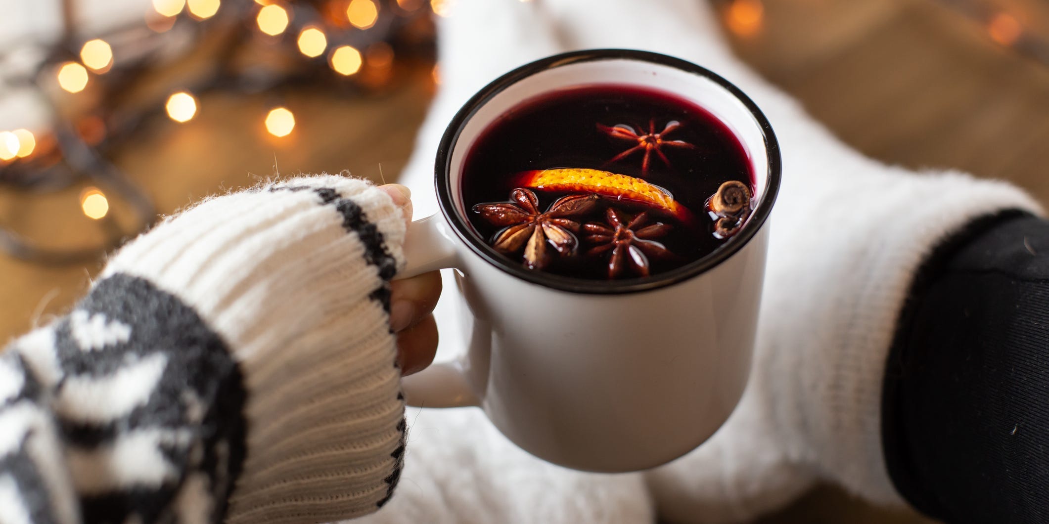 A person's hand holding a white mug full of mulled wine out in front of them