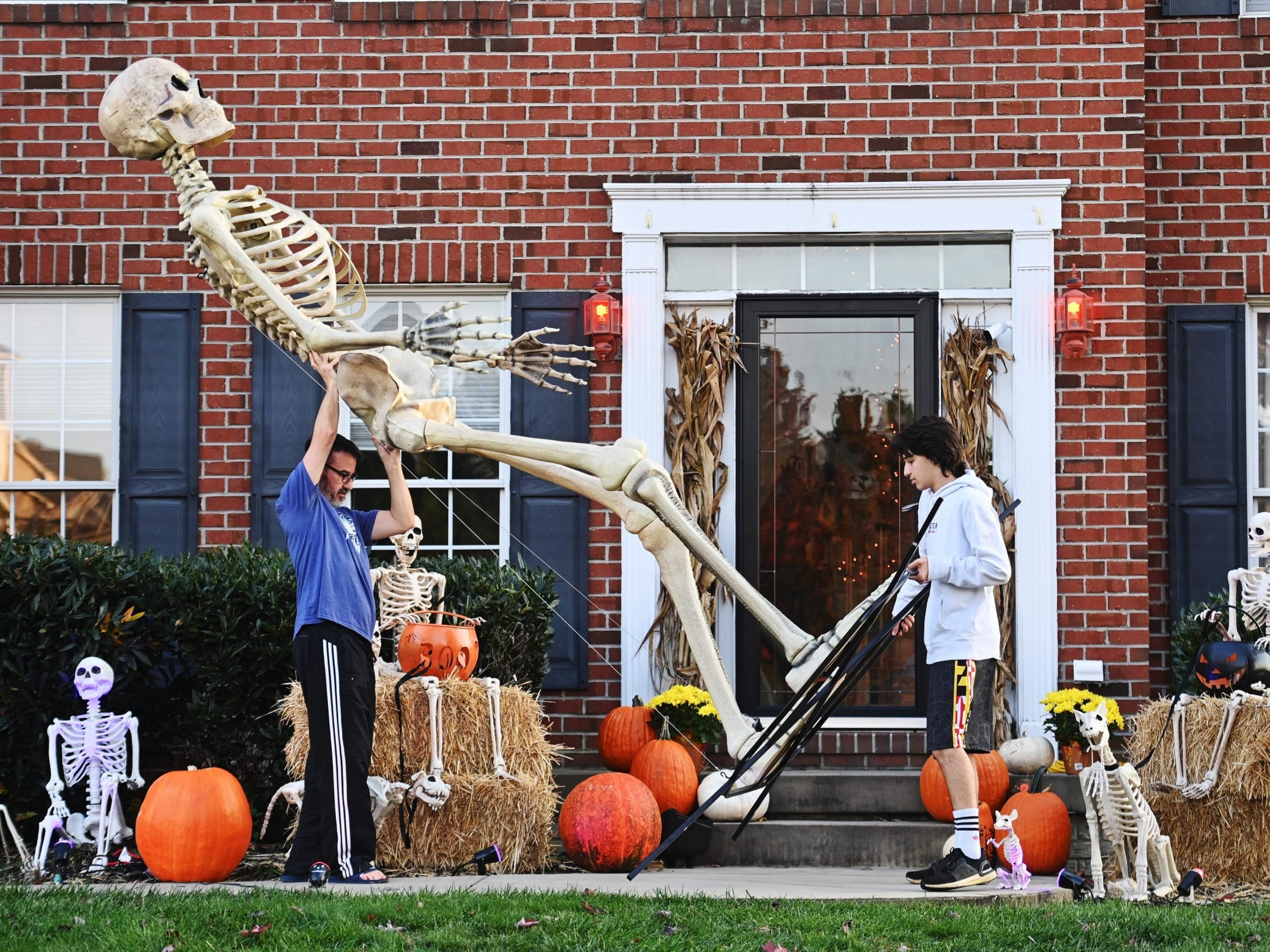 A father and son carry their 12-foot-tall Home Depot skeleton into storage after Halloween.