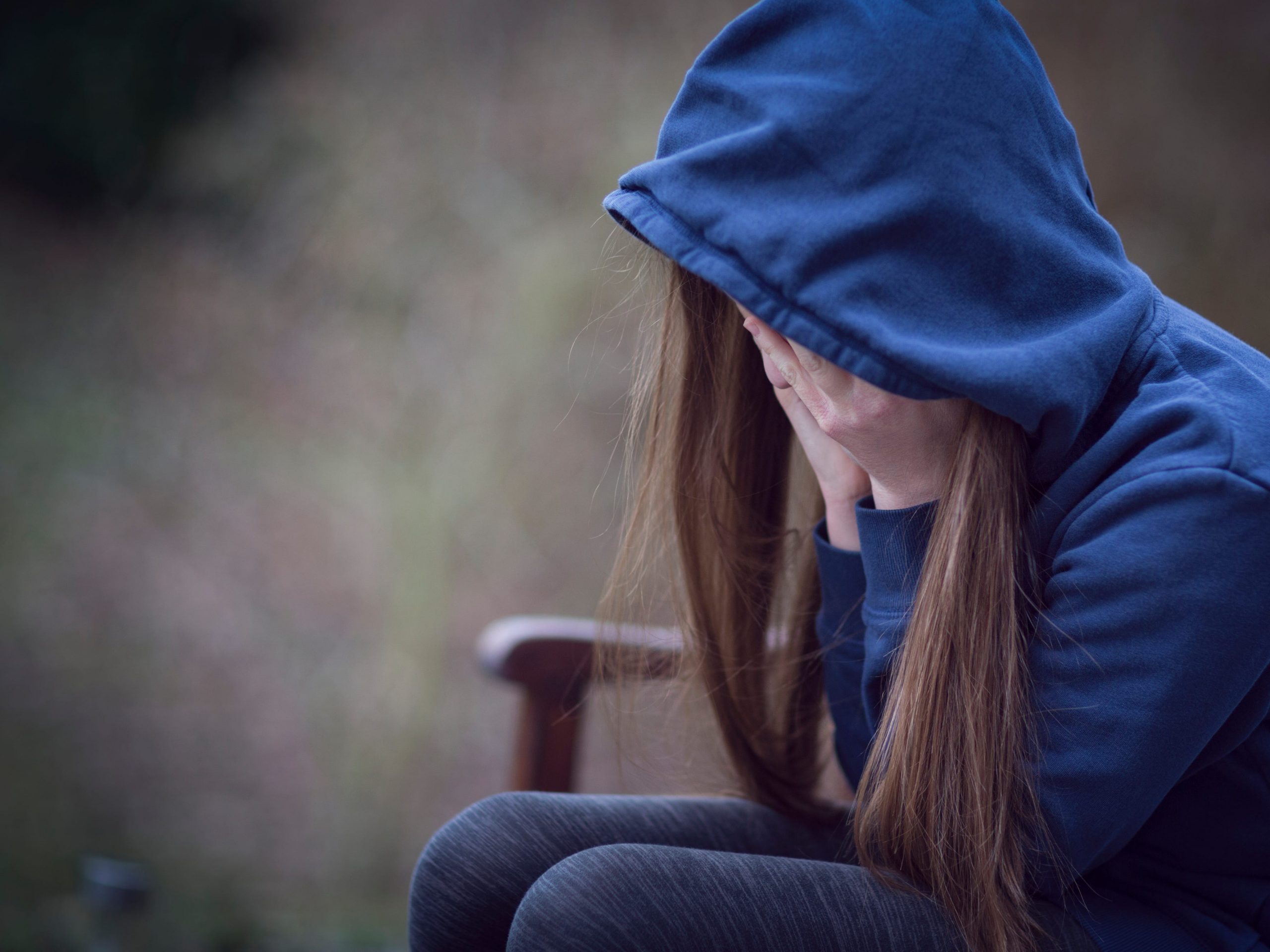 Teenage girl in hooded top, with head in hands in despair