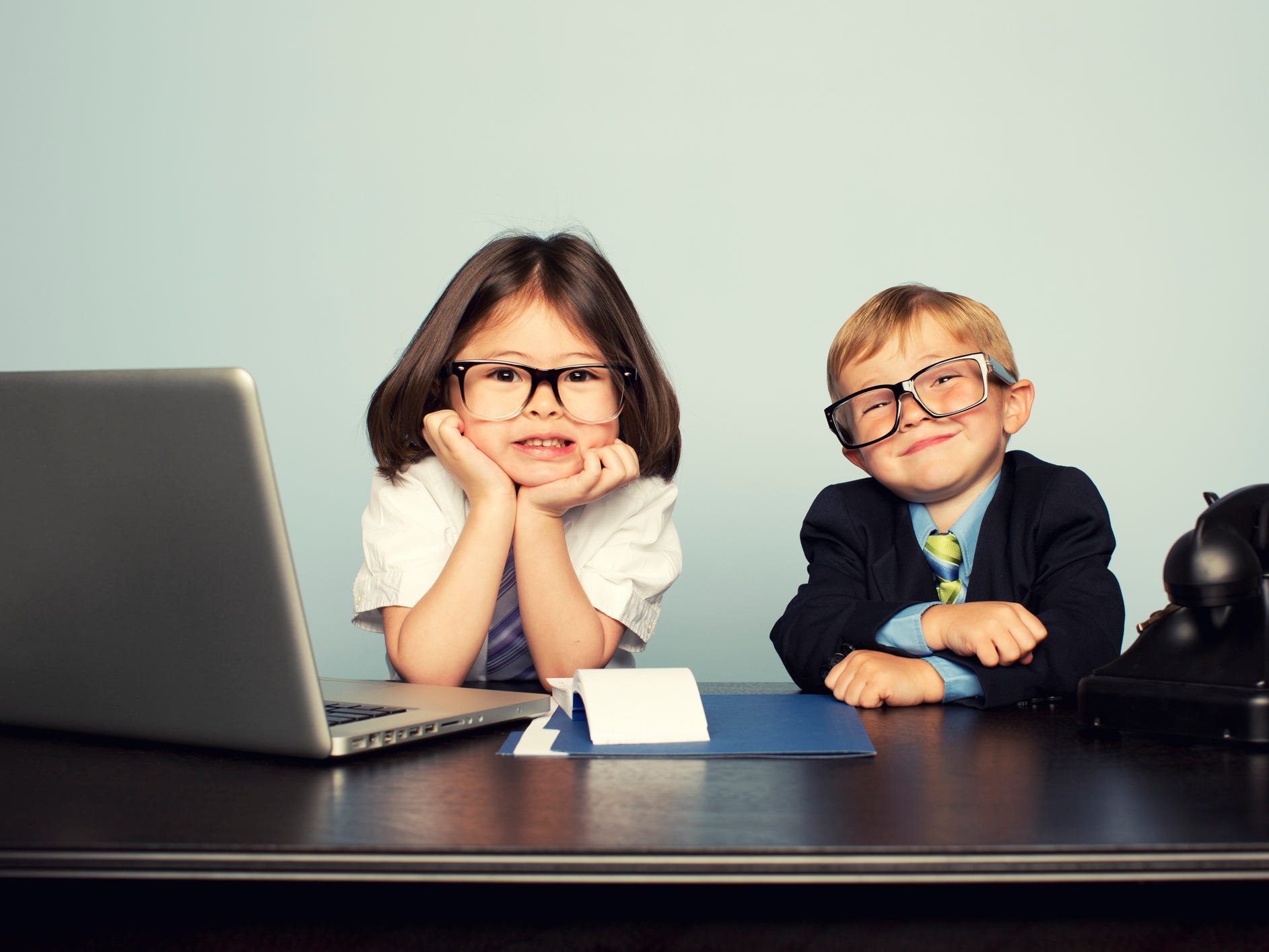 Two little kids dressed up like office goers with a phone and laptop.