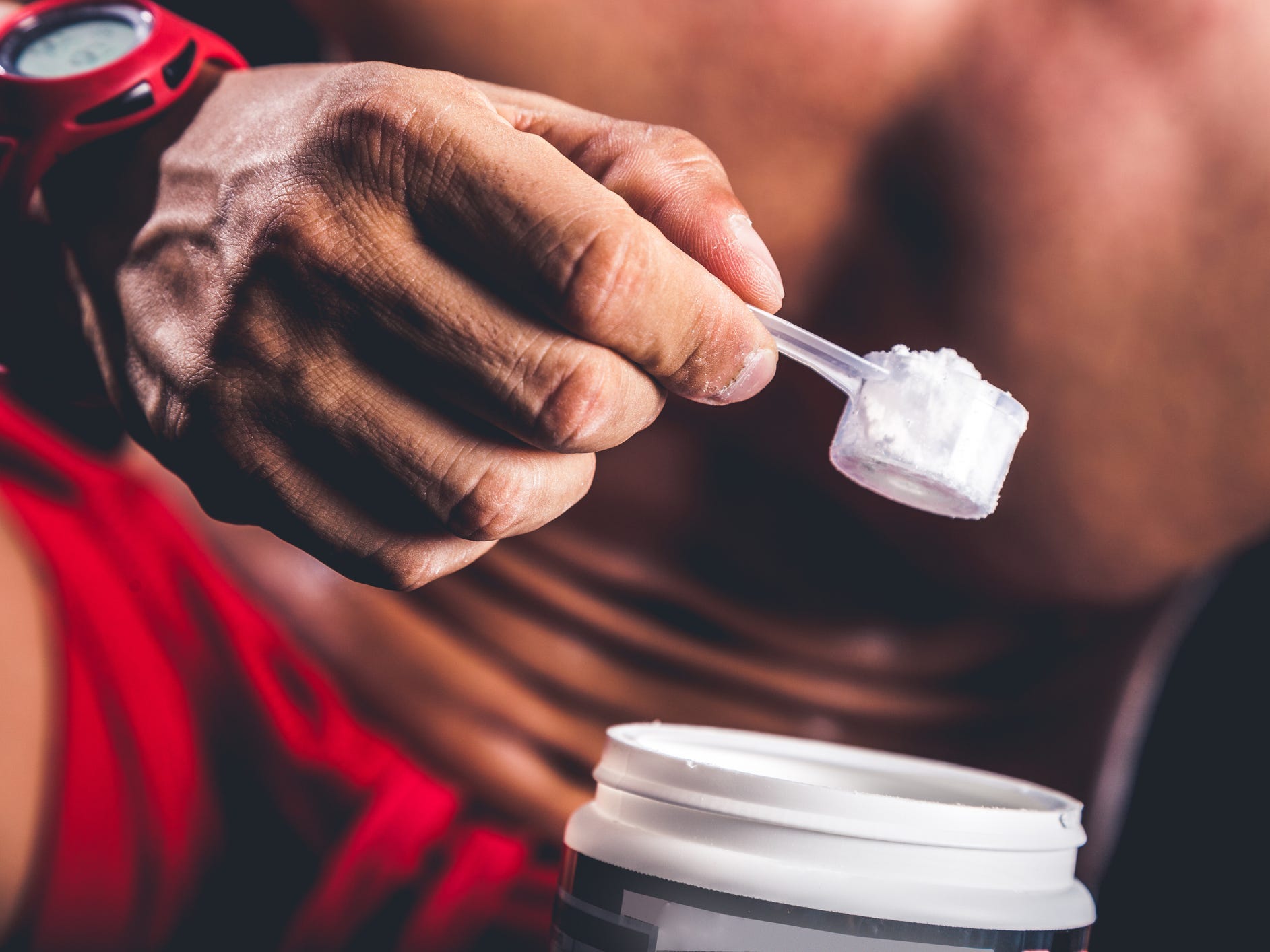 a close up of a shirtless, athletic person holding a scoop of preworkout supplement