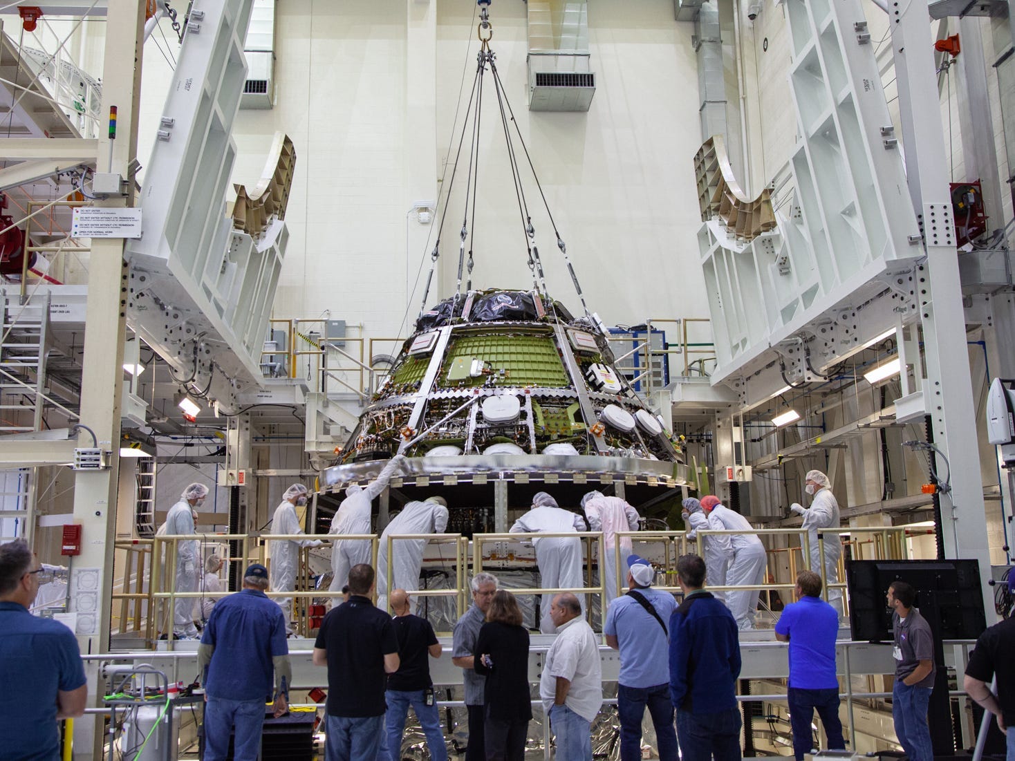 orion spaceship in white engineering facility surrounded by technicians in clean suits