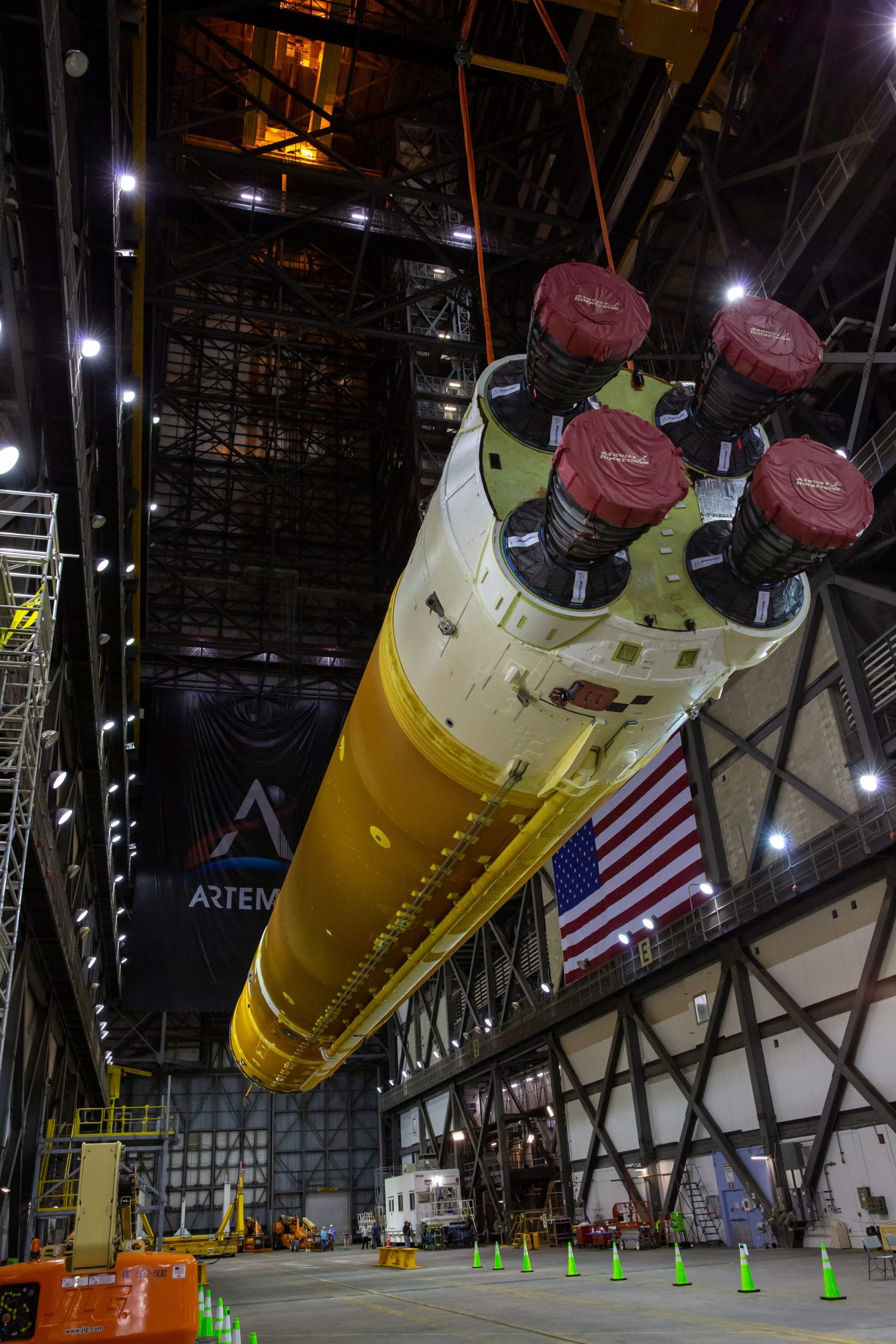 space launch system core stage orange rocket lifted in the air inside large rocket assembly facility