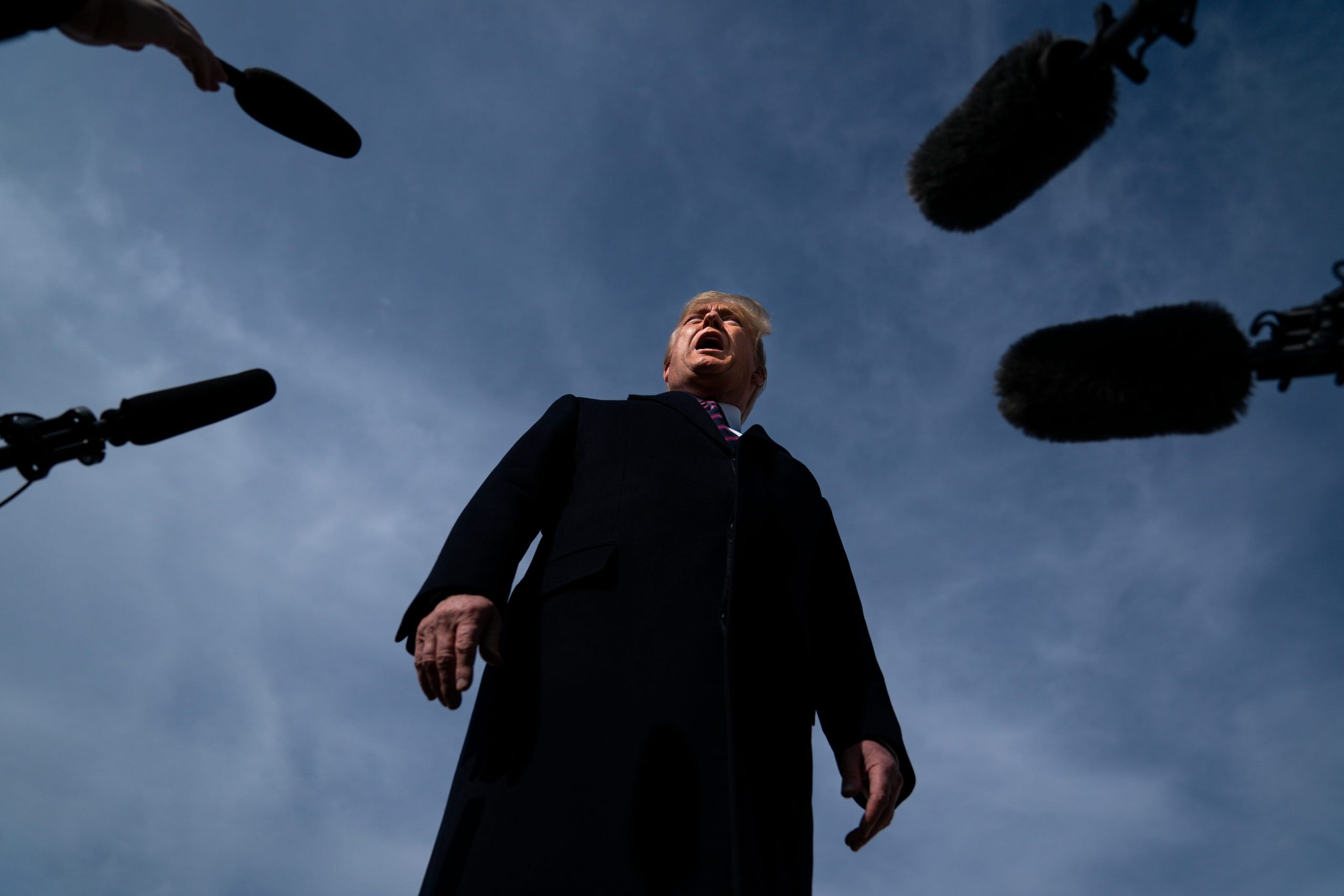 Former President Donald Trump in a black coat speaks into multiple microphones
