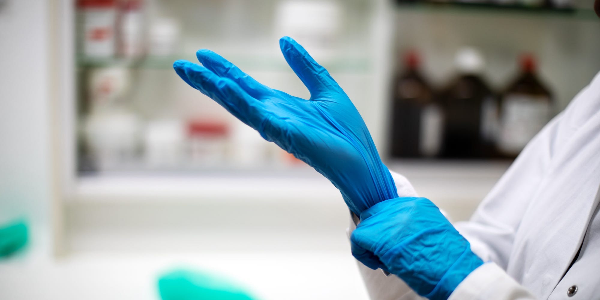 Close-up of a chemist putting on gloves in pharmacy.