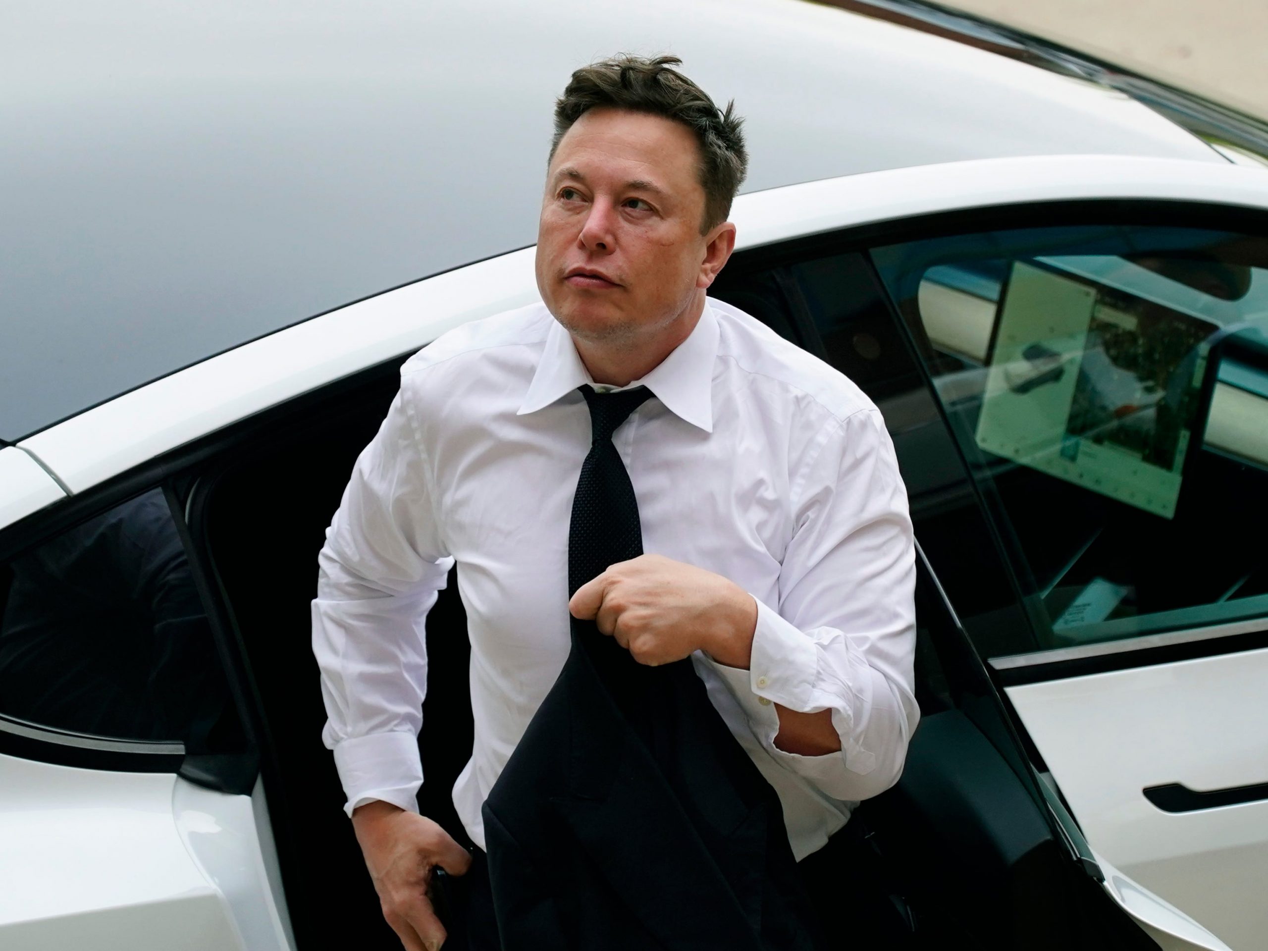 Tesla CEO Elon Musk in a white shirt and tie exits the backseat of a white Tesla