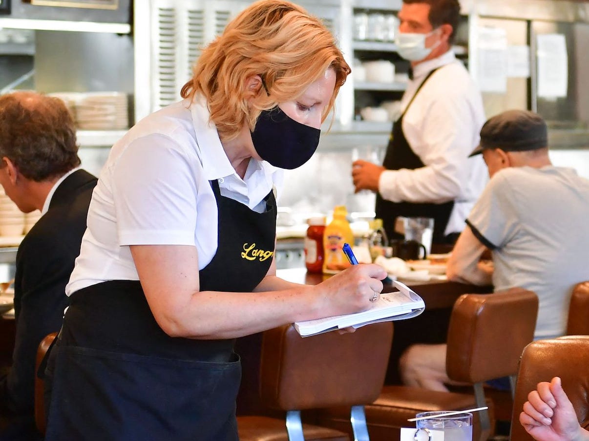 A waitress is taking a customer’s order at a table. There are other customers and another server in the background.