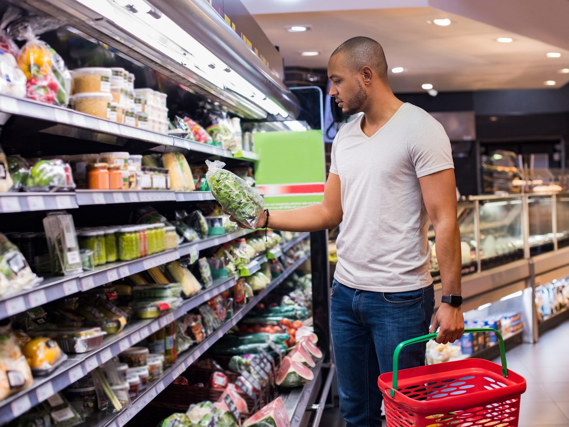 a grocery shopper holding a basket and examining a calorie label in the produce aisle of a grocery store