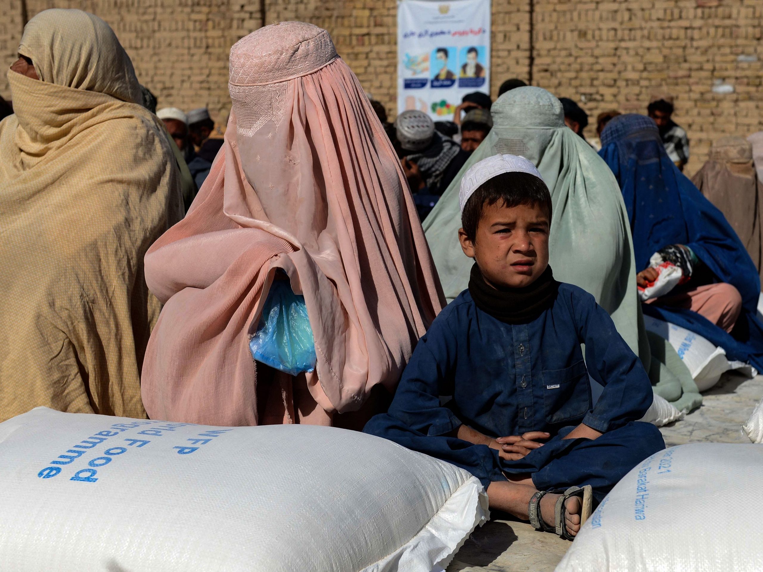 Afghan people sit besides sacks of food grains distributed as an aid by the World Food Programme (WFP) in Kandahar on October 19, 2021.