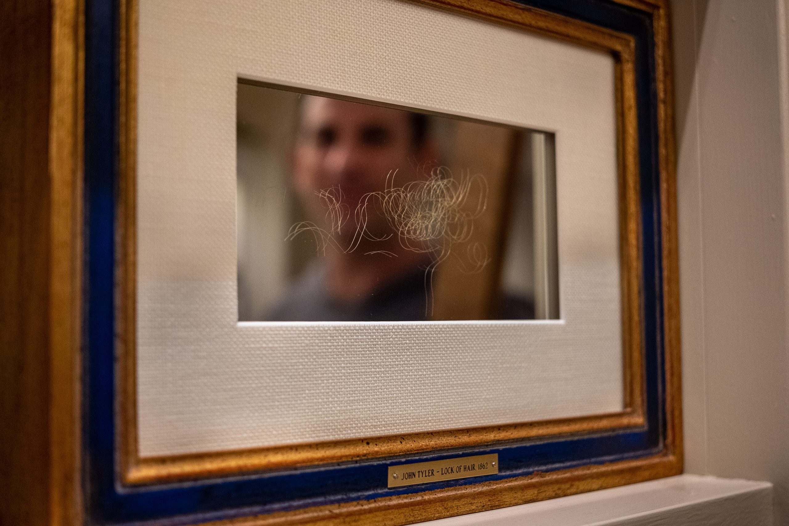 Hair is seen in a frame, under the reflection of a man's face.