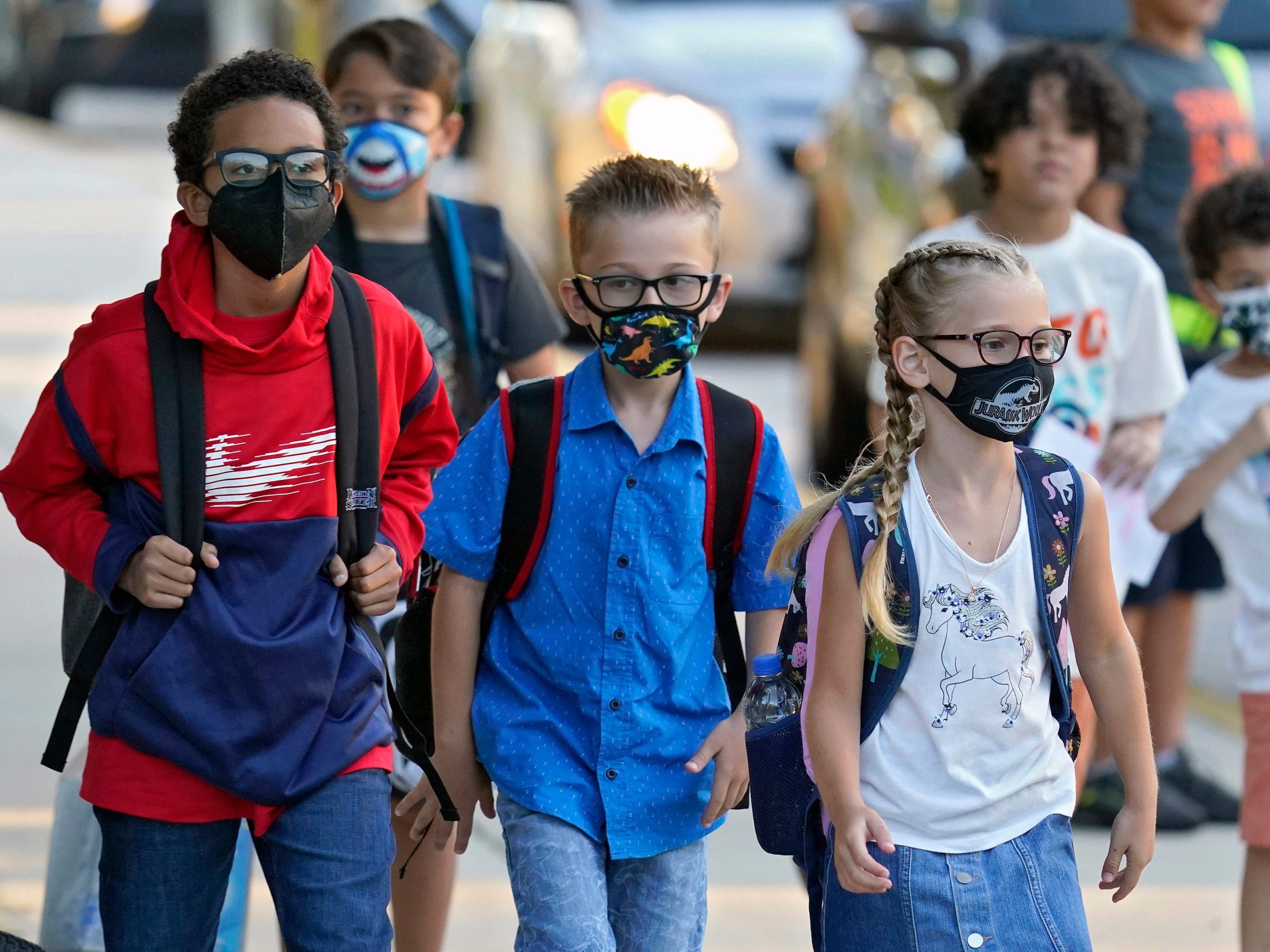 A group of kids wearing masks and backpacks walk toward their classrooms.
