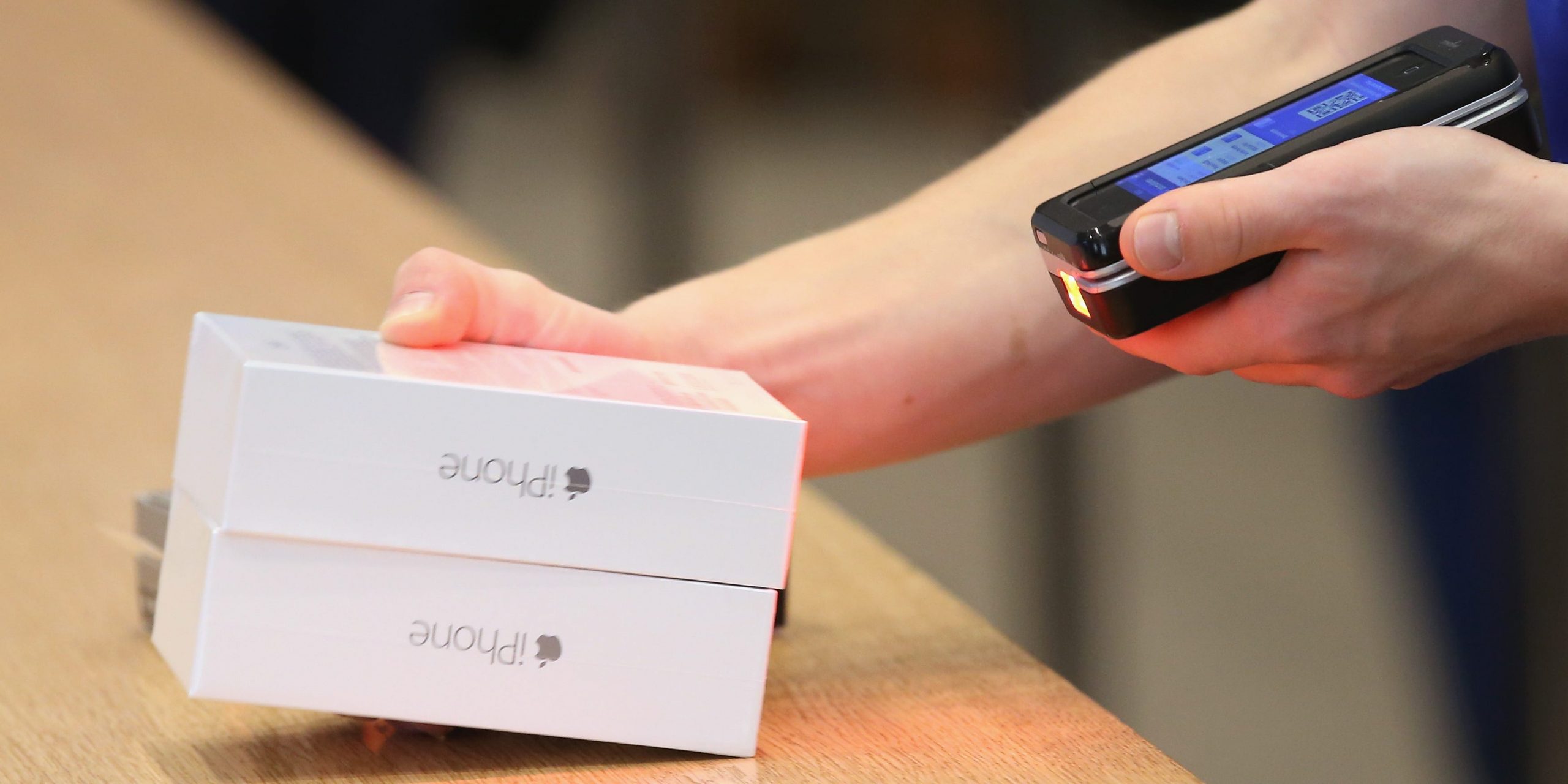 Close up of an Apple Store employee's hands holding two new iPhone boxes and scanning them with a special handheld sales device.